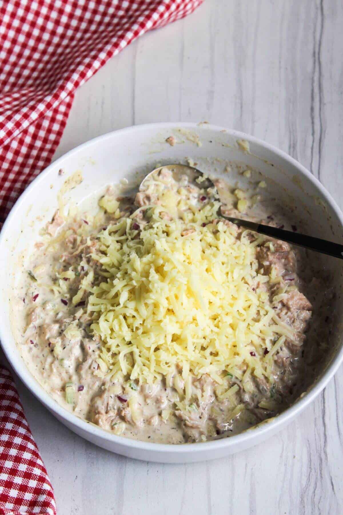 Mozzarella cheese added to tuna and mayonnaise mixture in bowl.