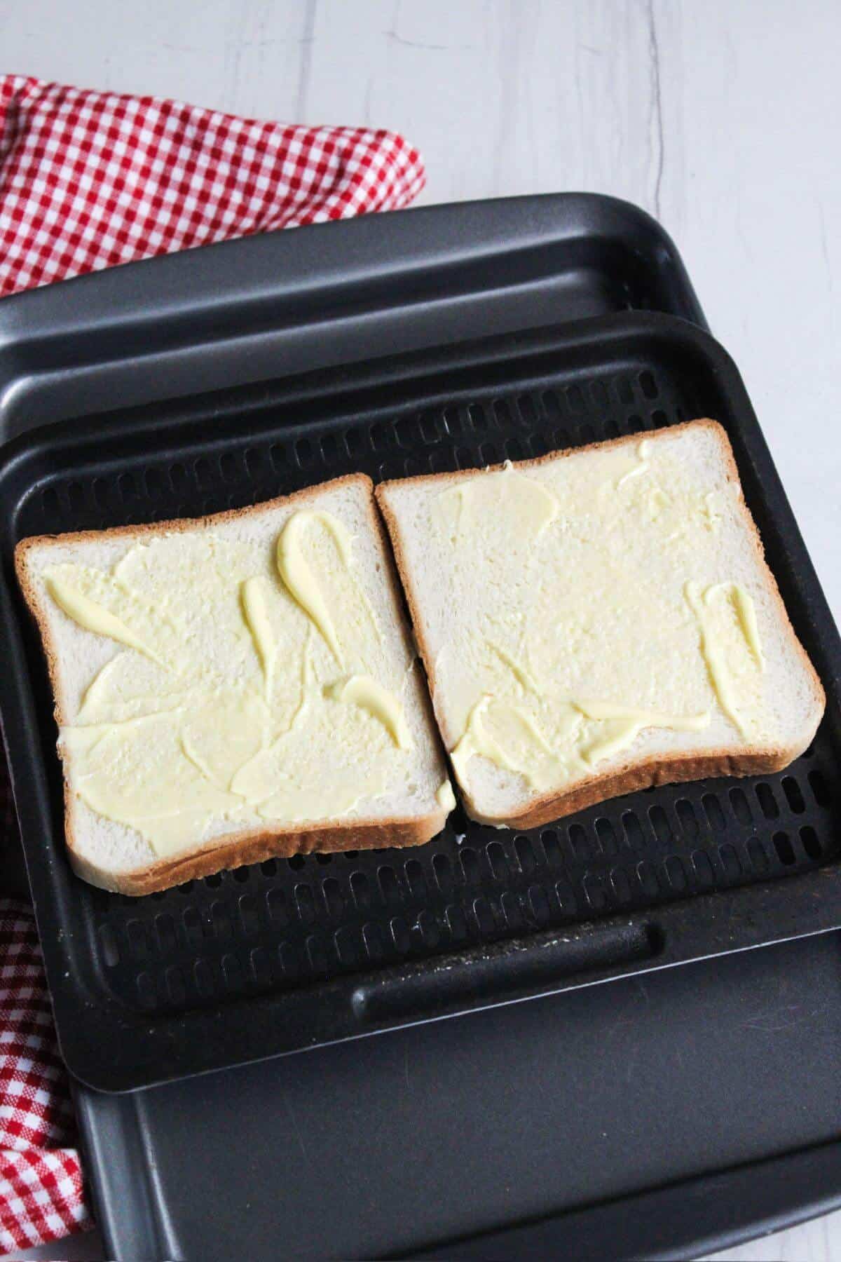 Two slices of buttered bread on air fryer tray.