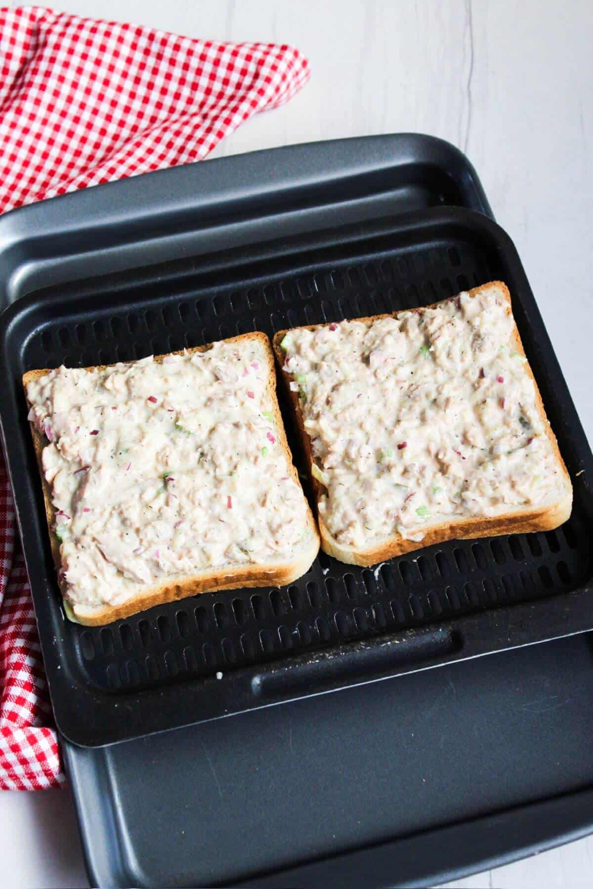 Two slices of bread topped with tuna mixture on air fryer tray.