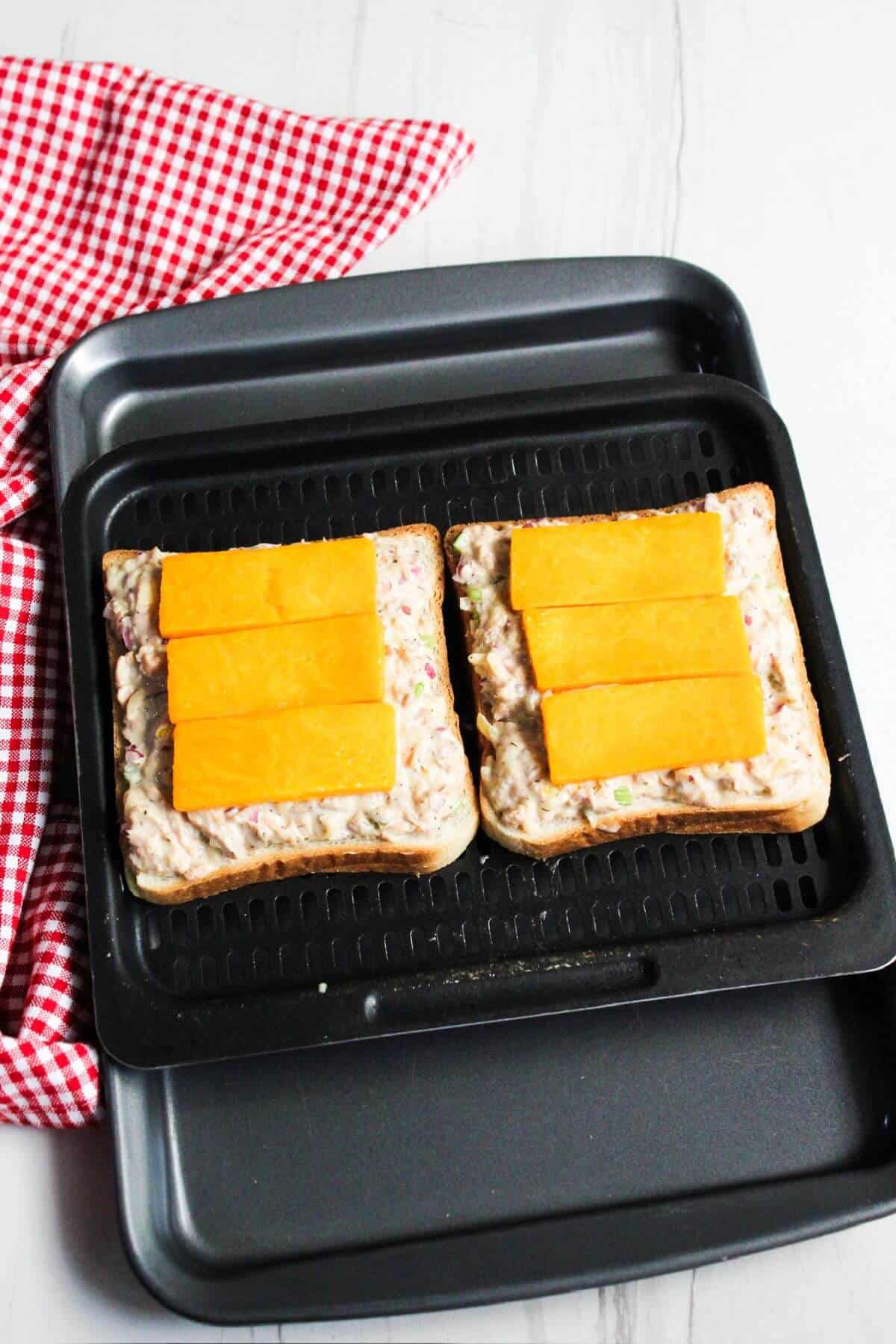 Two slices of bread topped with tuna and cheese on air fryer tray.