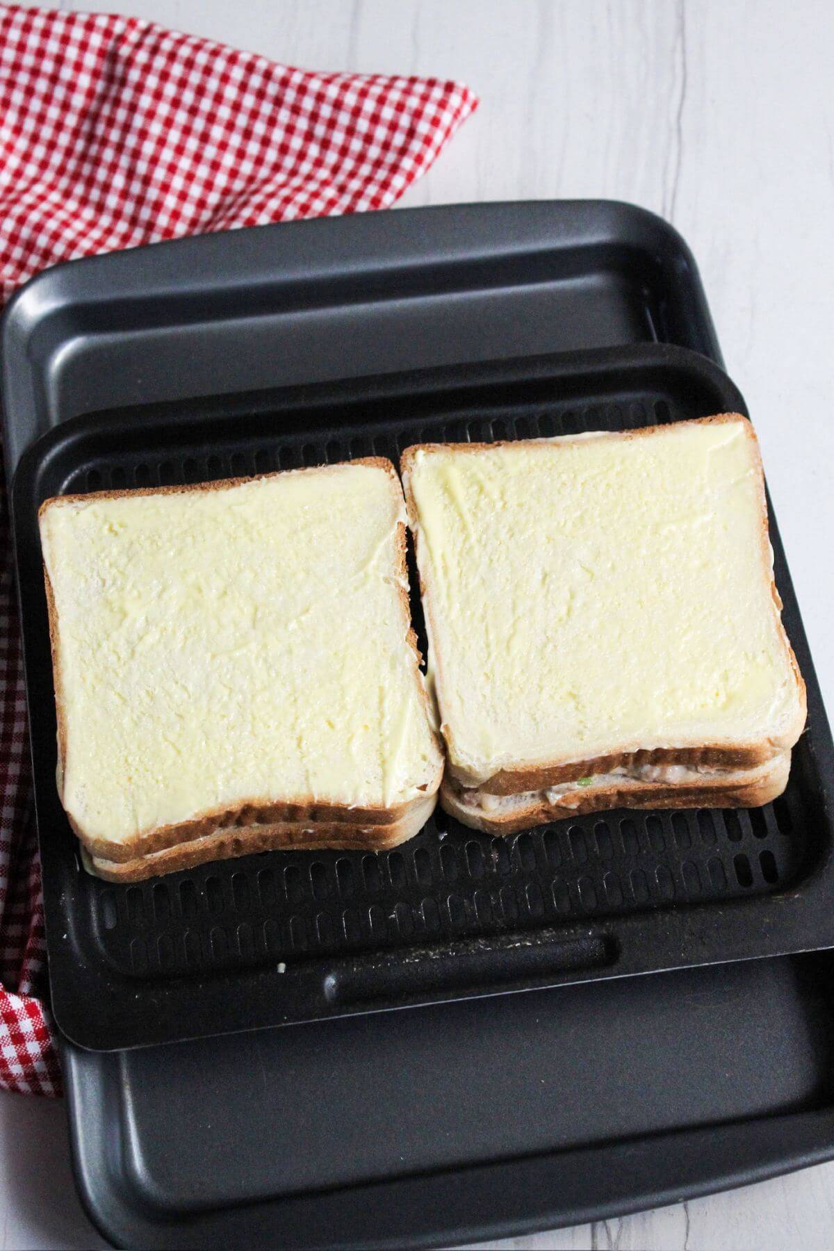 Two assembled buttered tuna sandwiches on an air fryer tray.