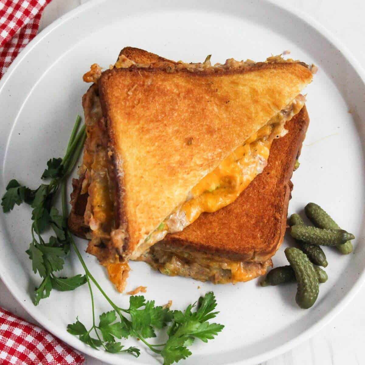 A tuna melt sandwich on a plate with pickles.