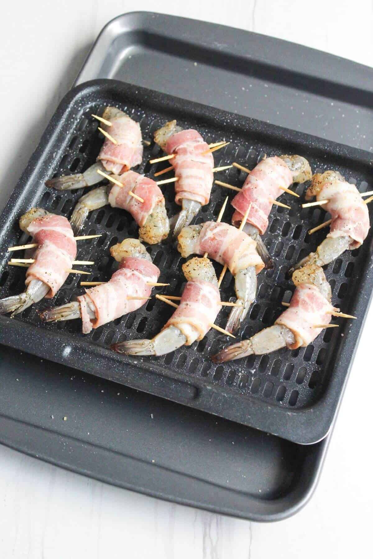 Bacon wrapped shrimp on an air fryer tray sheet.