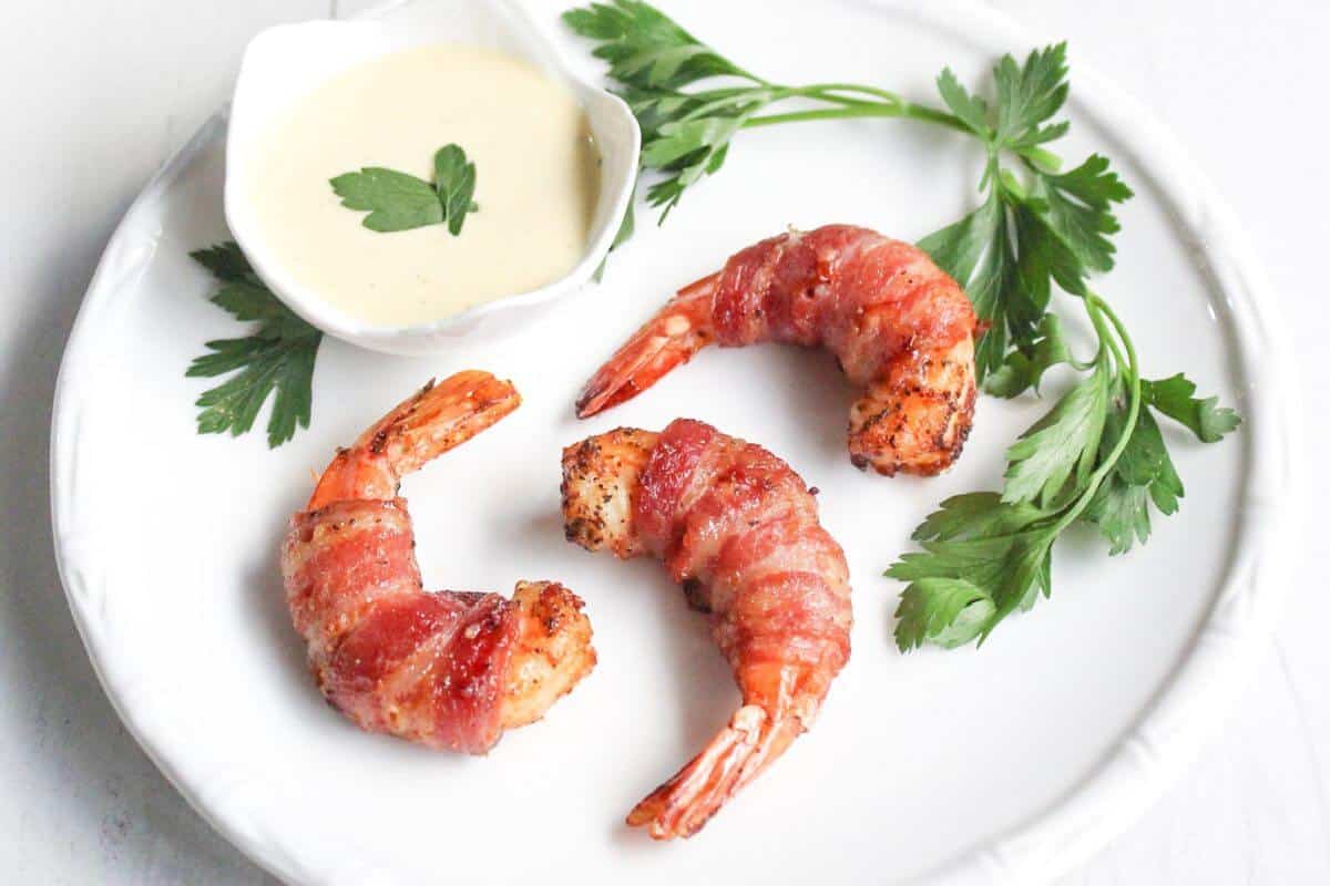 Bacon wrapped shrimp on a white plate with dipping sauce.