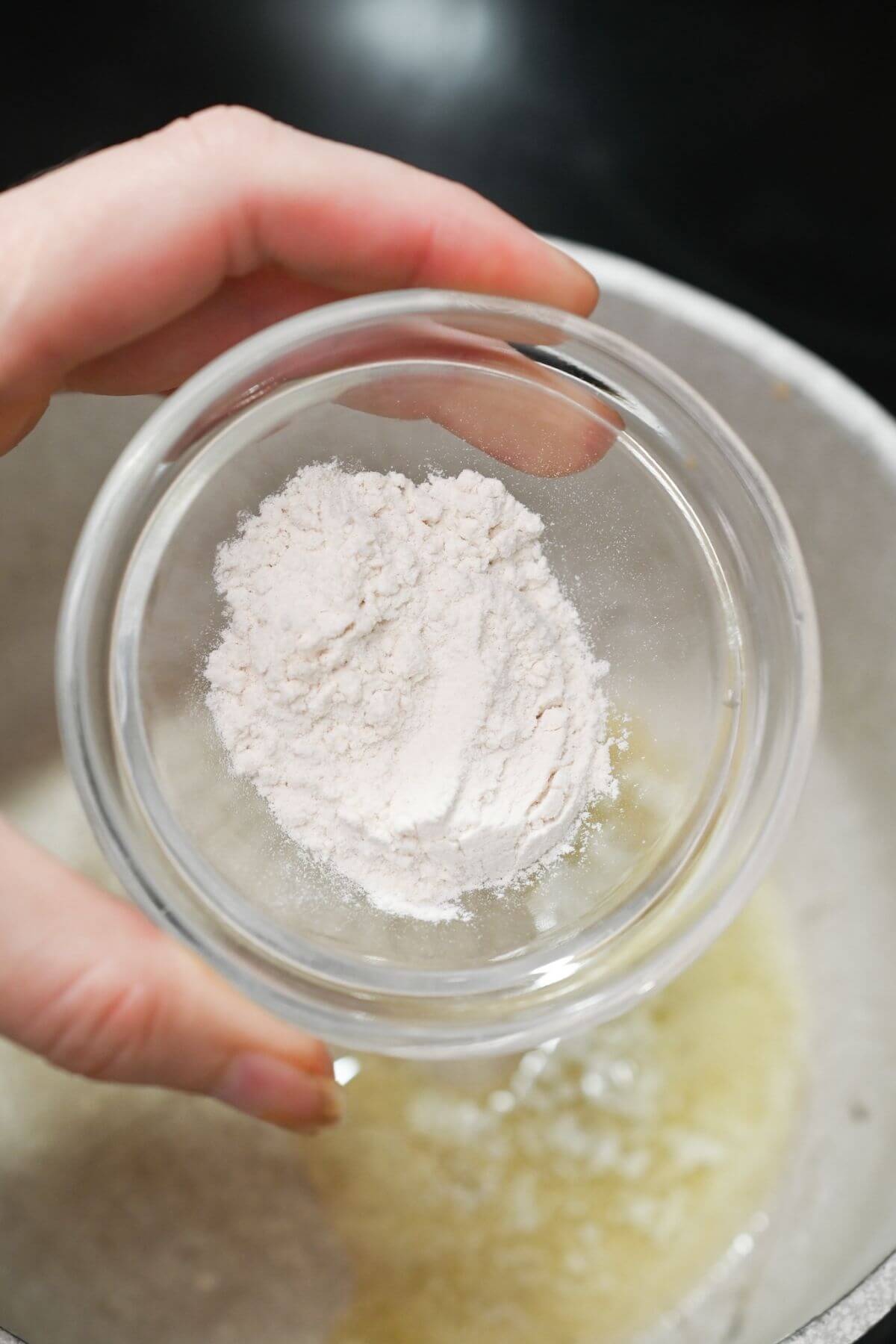 A person holding a bowl of flour over melted butter.