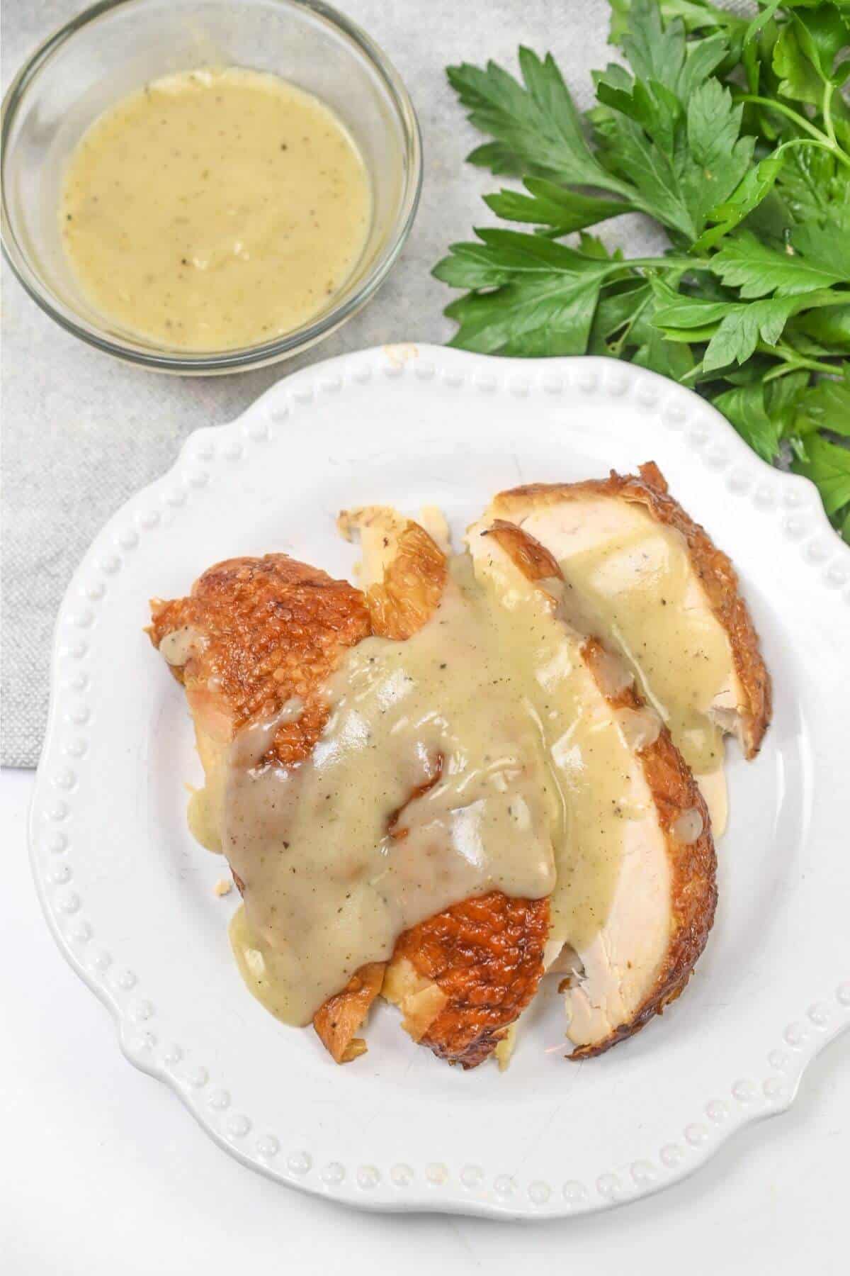 Chicken breast with gravy and parsley on a white plate.