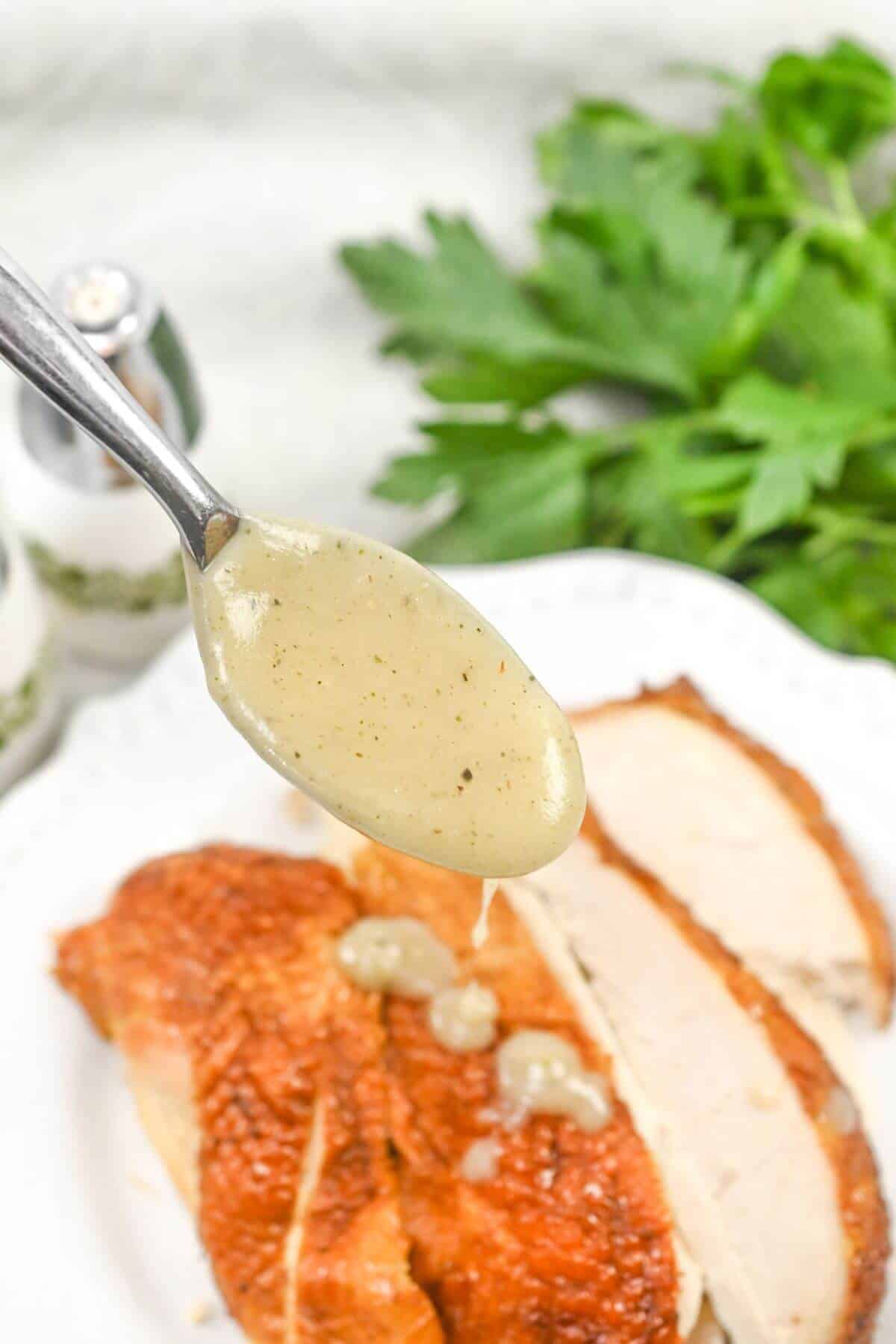 A spoon is drizzling gravy over a piece of chicken.