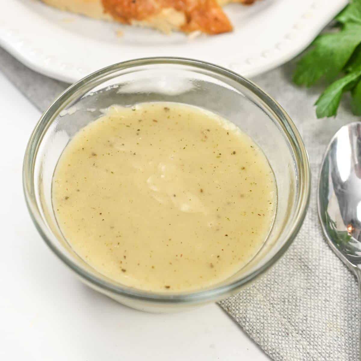 A bowl of gravy with a spoon next to a slice of bread.