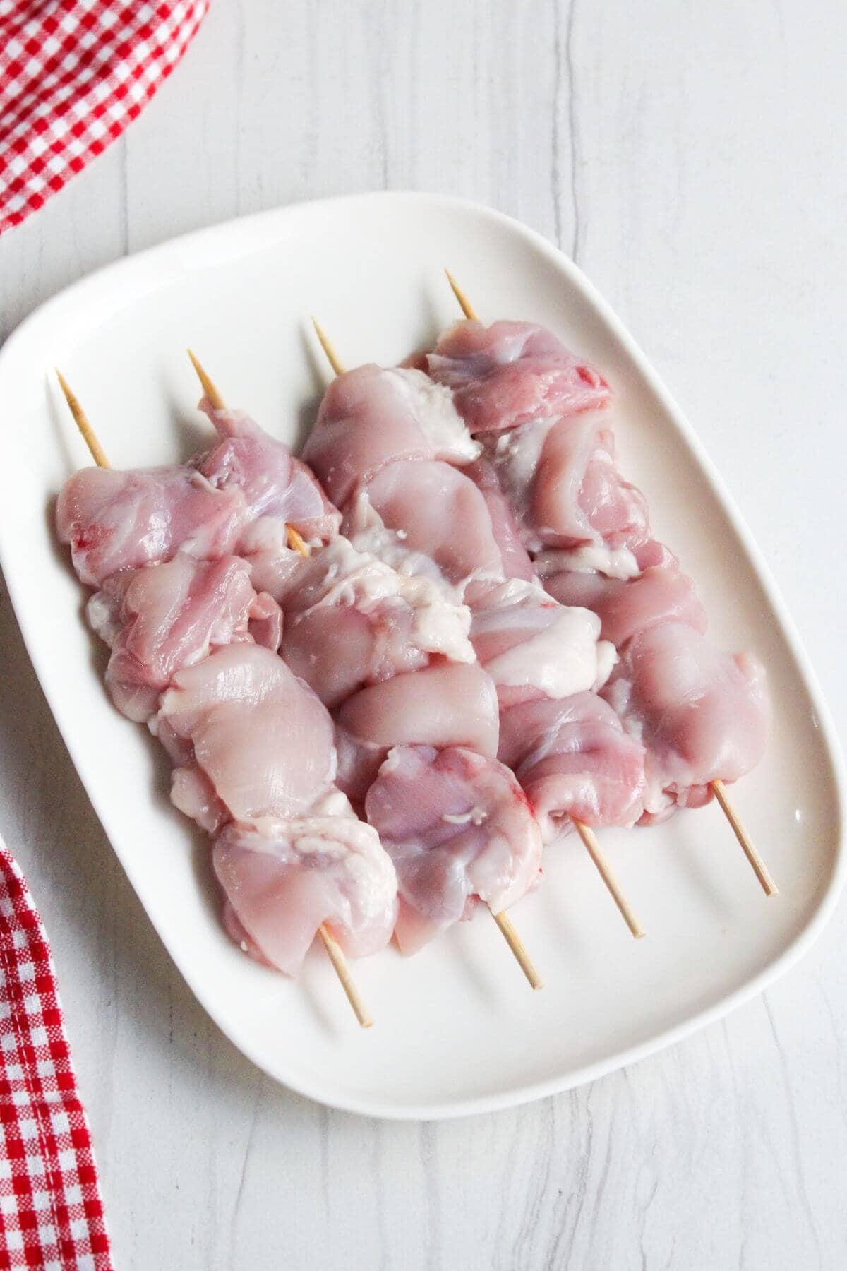 Chicken thigh meat on skewers on a white plate.