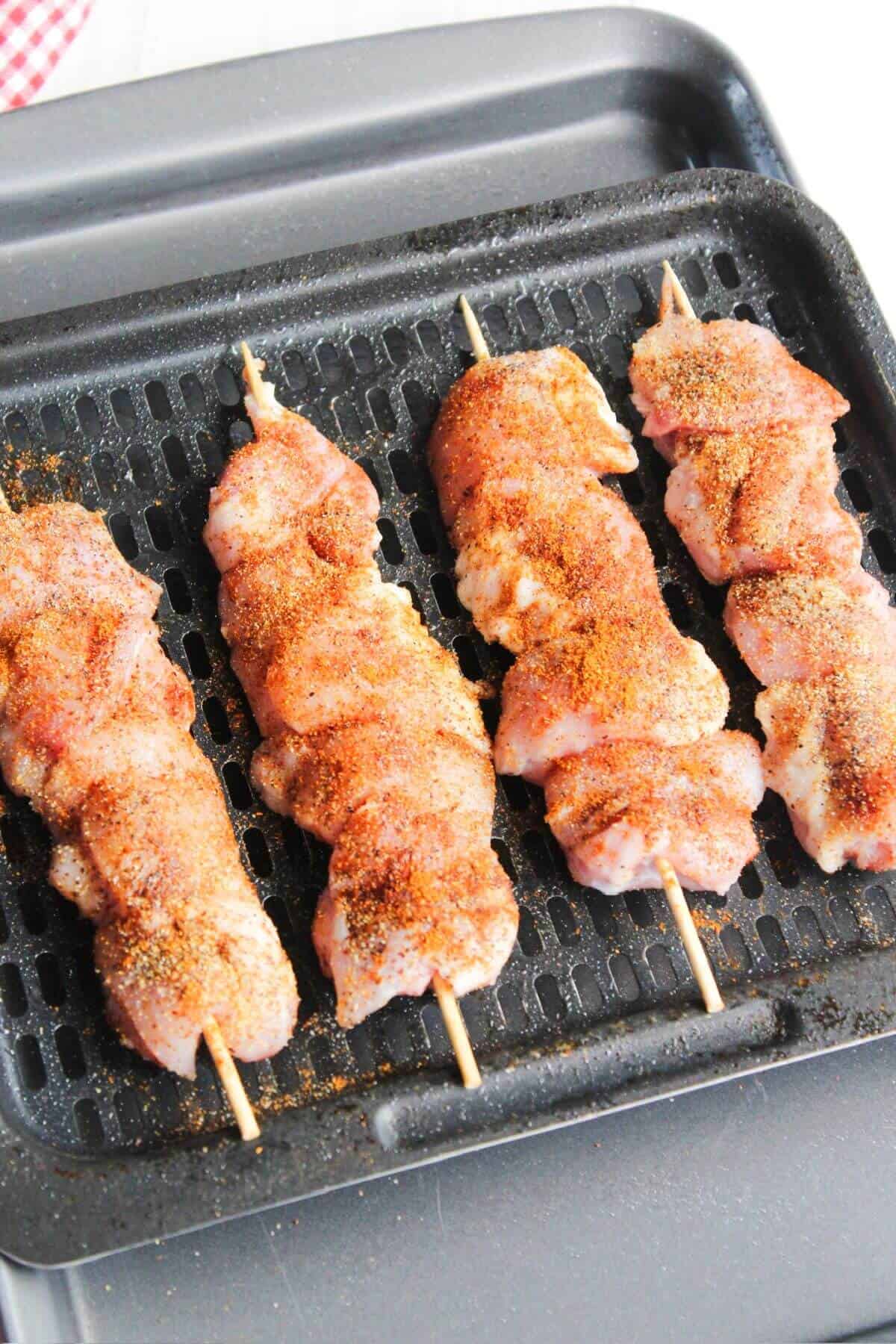 Prepared chicken skewers on air fryer tray.