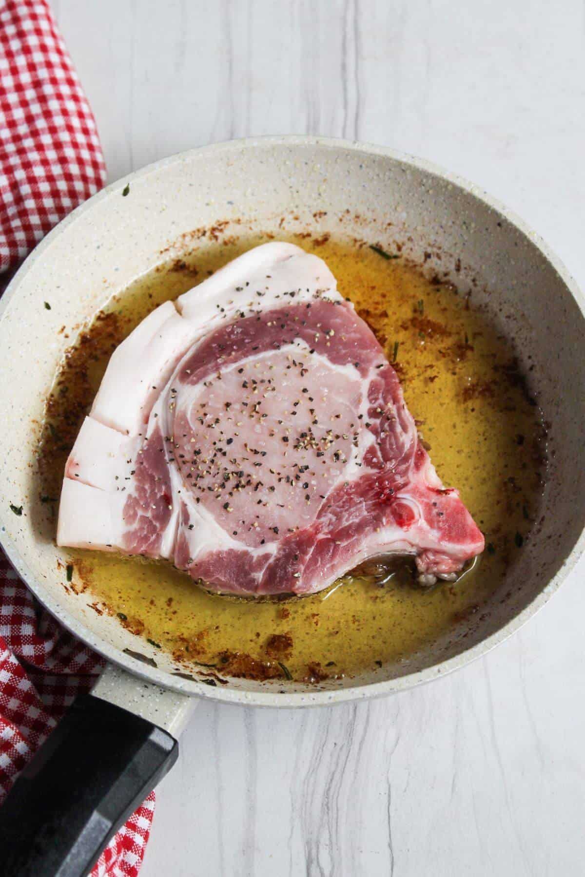 A bone-in pork chop is cooked in a frying pan.