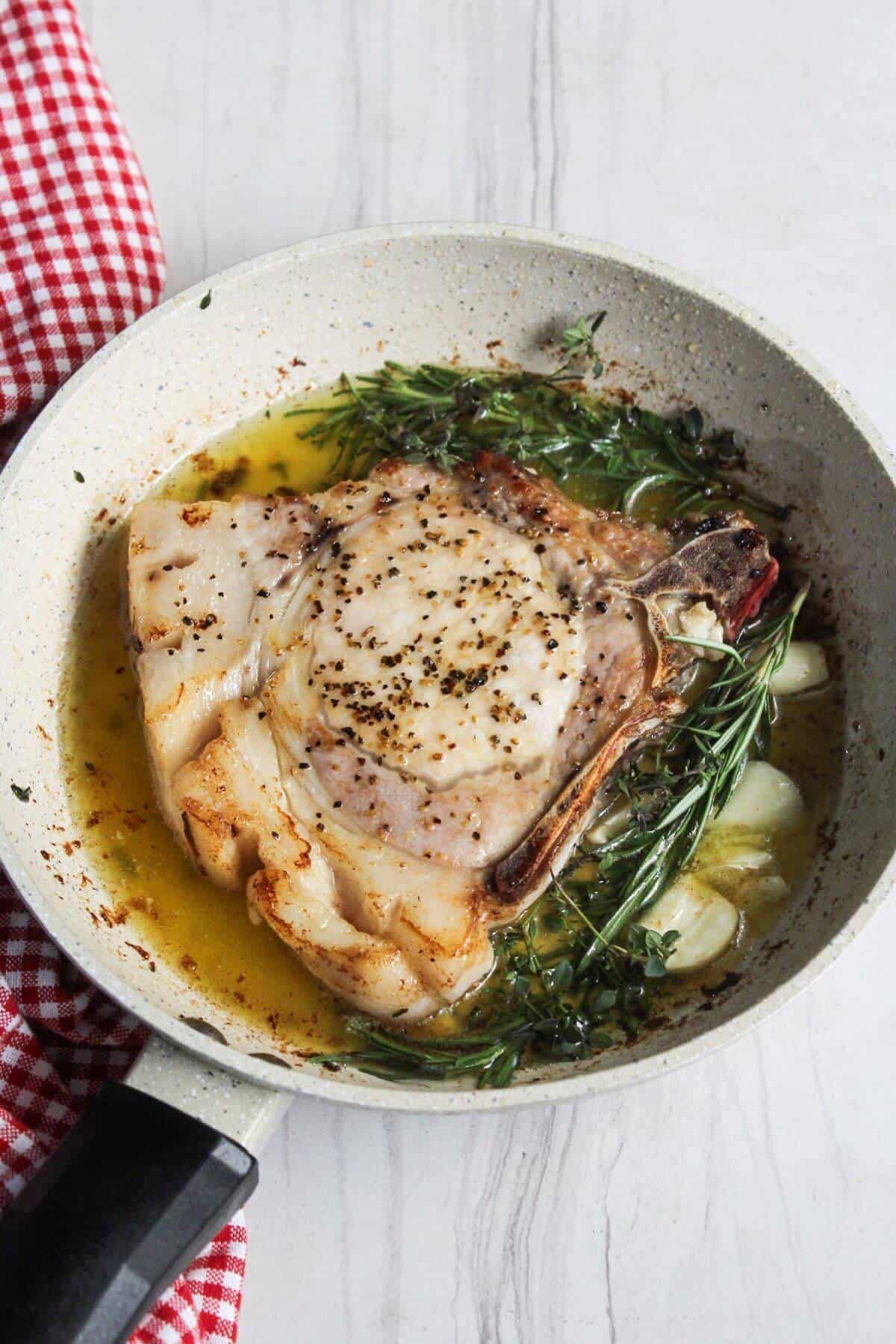 Pork chop in a pan with herbs and garlic.