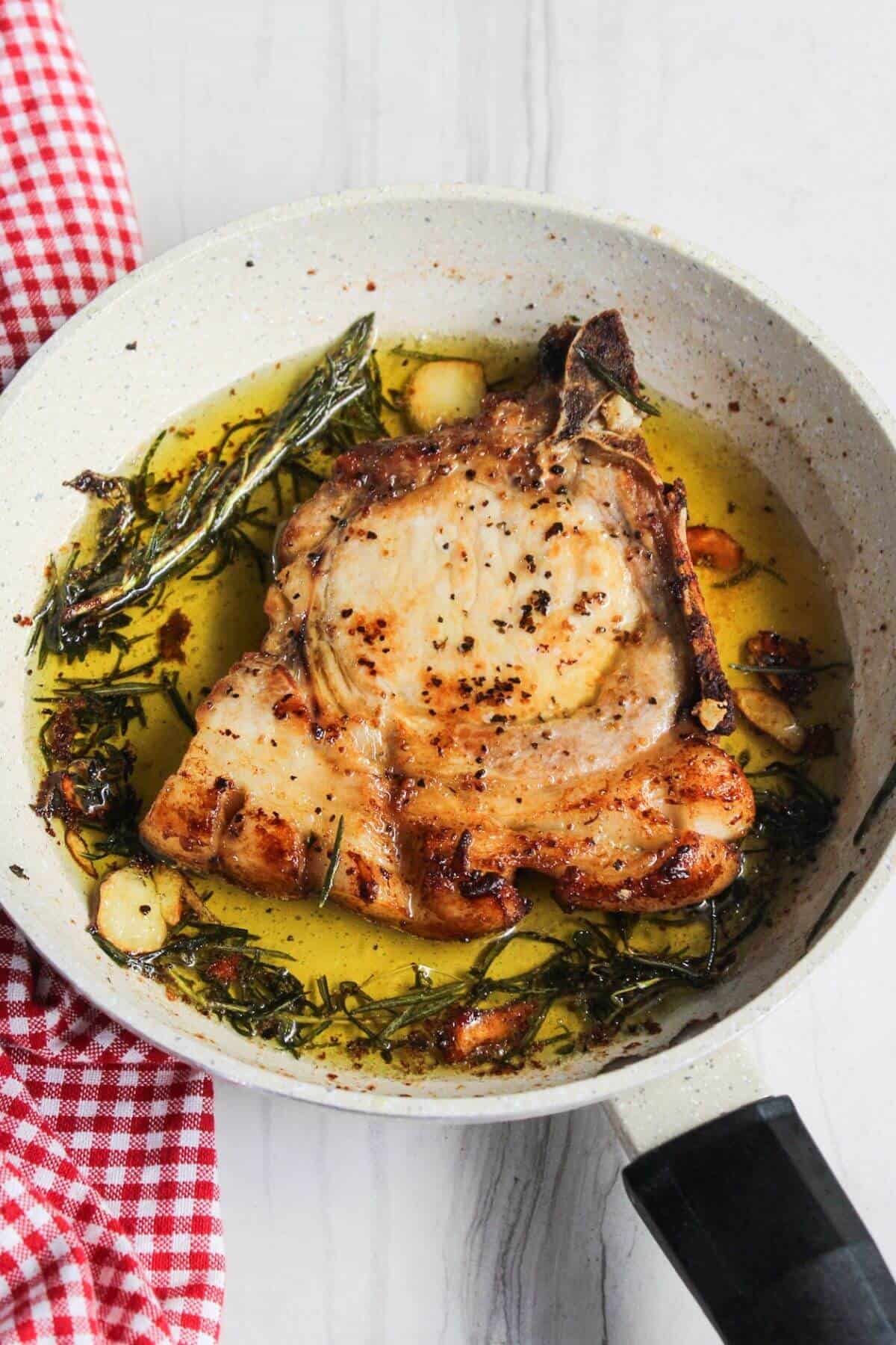Pork chop in a frying pan with herbs and garlic.
