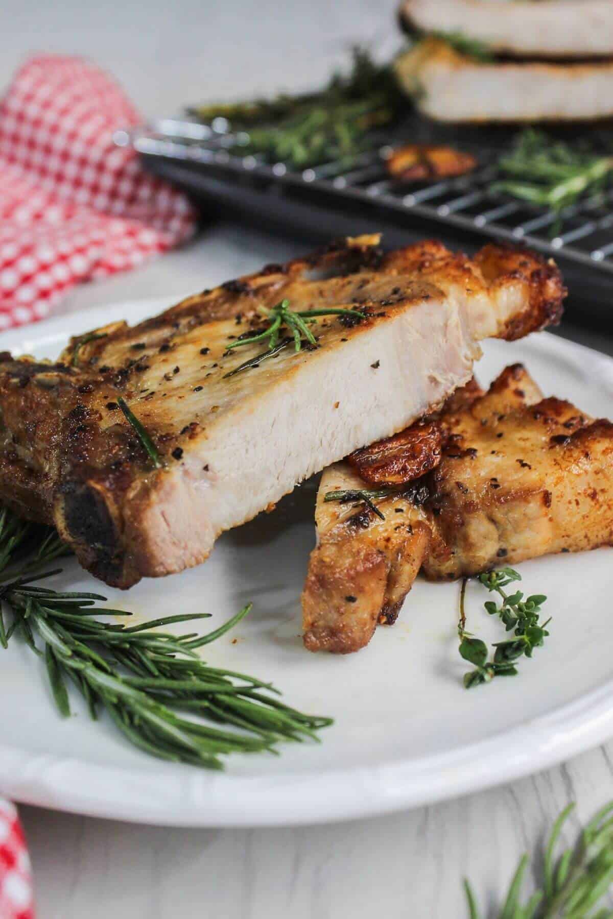 Pan-fried pork chops on a plate with rosemary sprigs.