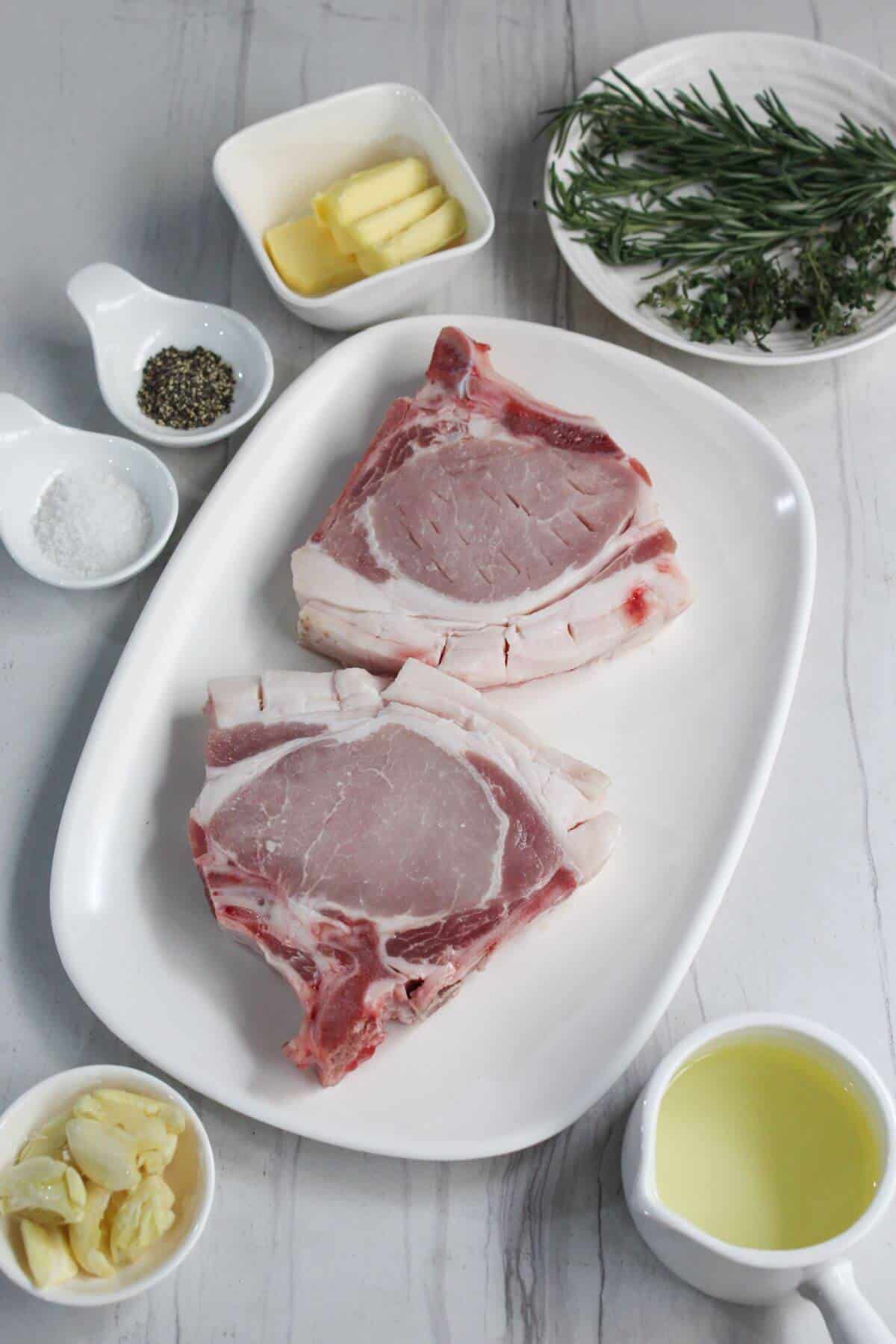 Pork chops on a white plate with herbs and spices.