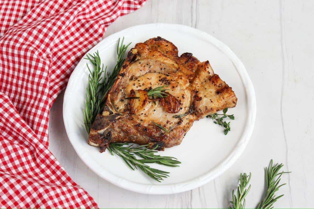 Pork chops on a plate with rosemary sprigs.