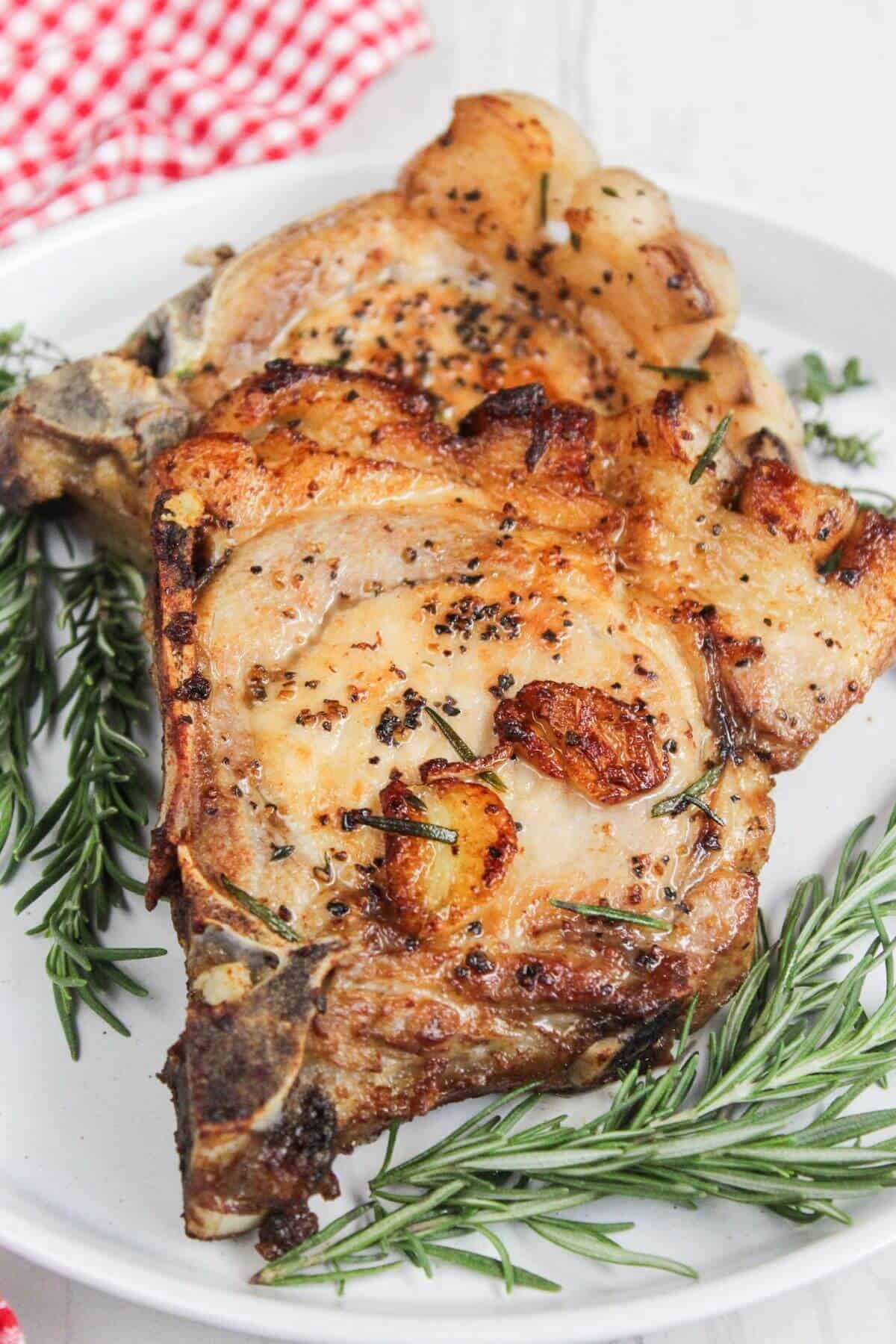 Pork chops on a white plate with rosemary sprigs.