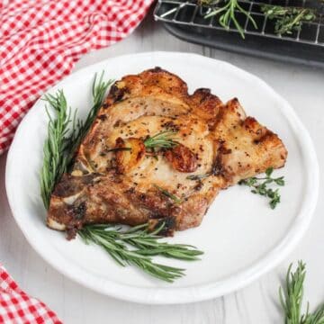 Pork chop on a plate with rosemary sprigs.