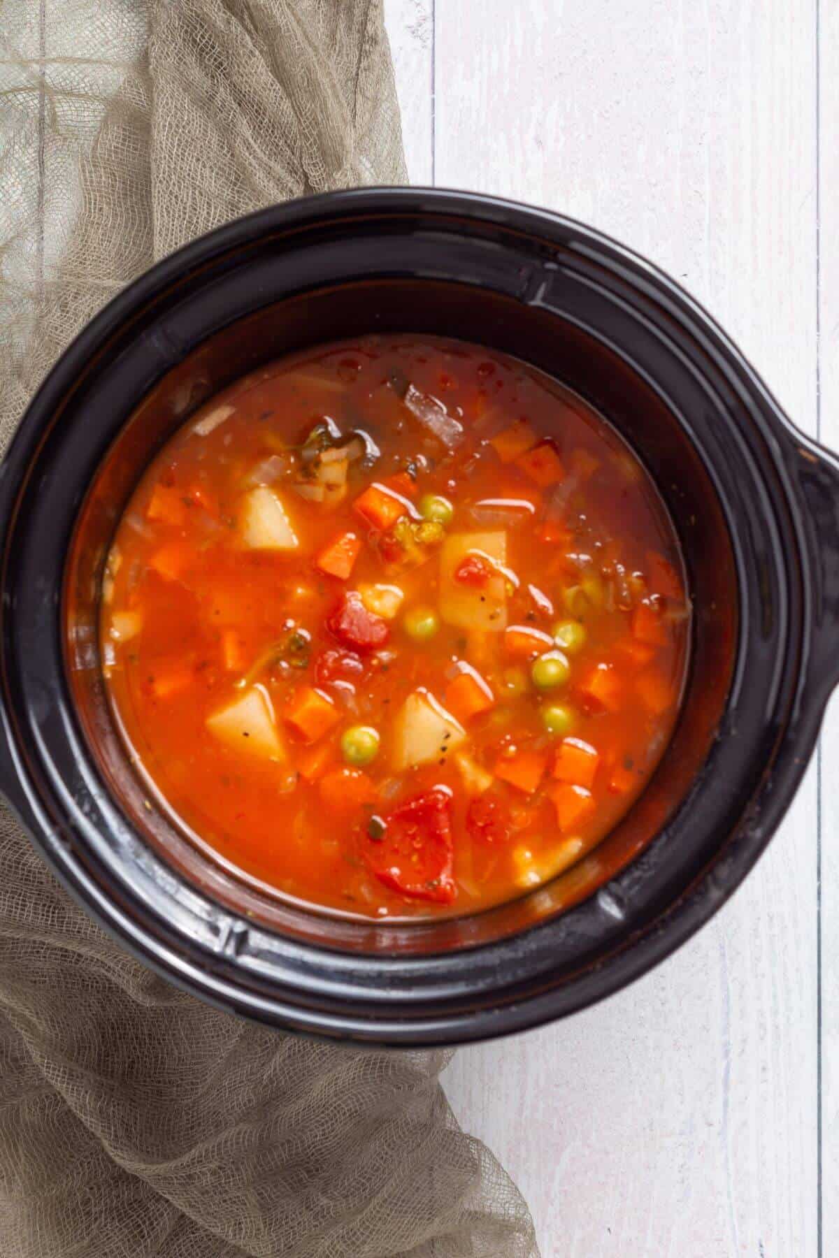 A crock pot of vegetable soup on a wooden table.