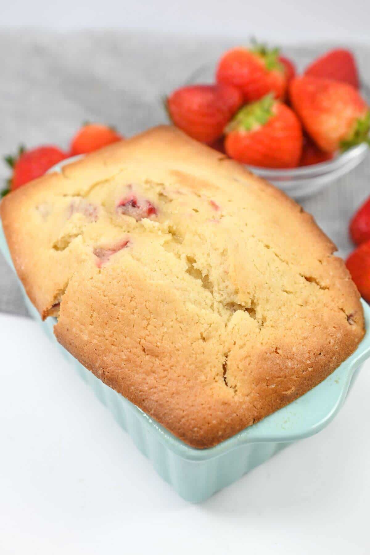 A loaf of strawberry pound cake in a loaf pan next to strawberries.
