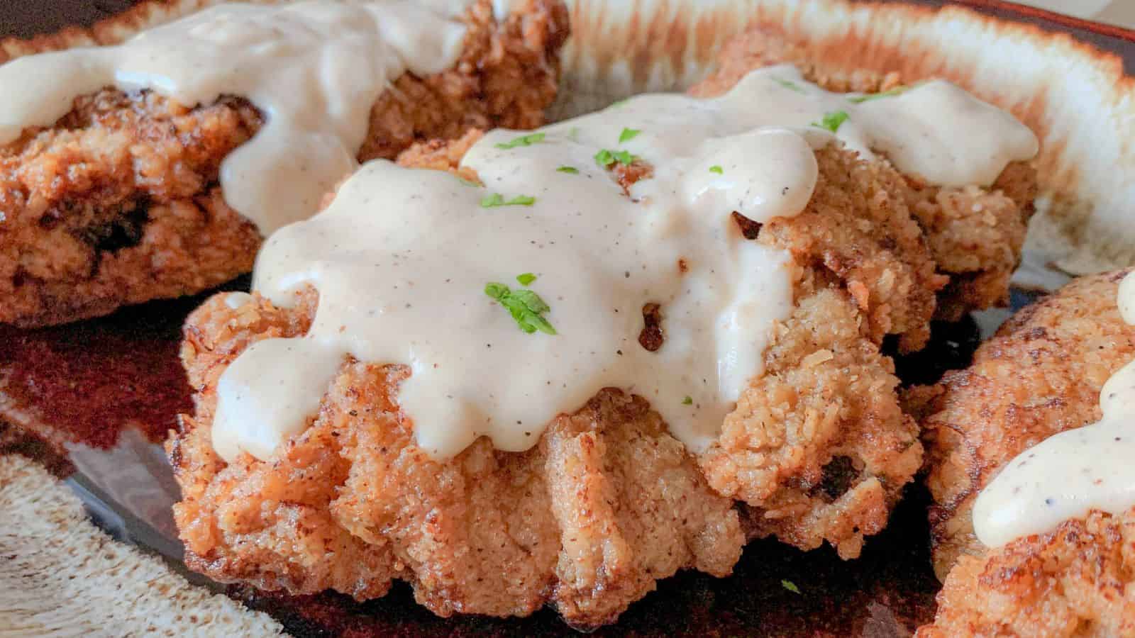 Country fried steaks on a platter smothered in white gravy.