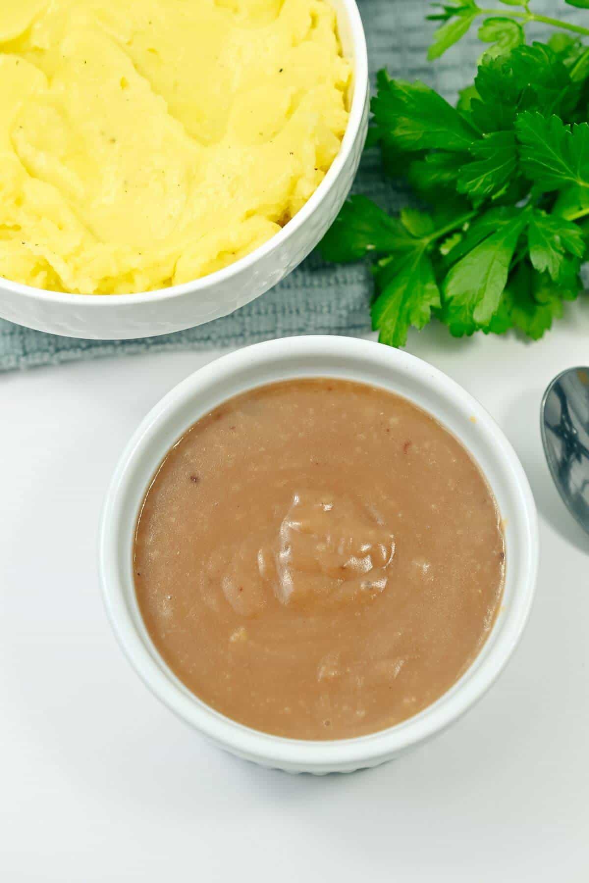 A bowl of gravy next to a bowl of mashed potatoes.