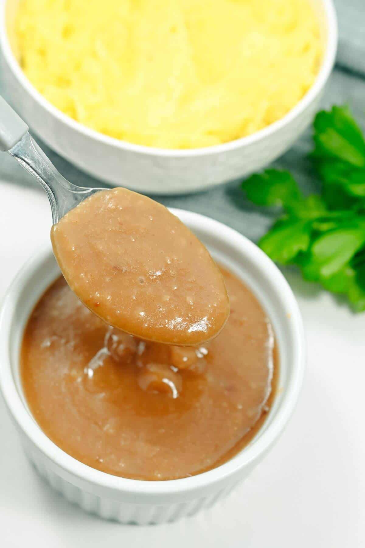 A bowl of gravy with a spoon in it.
