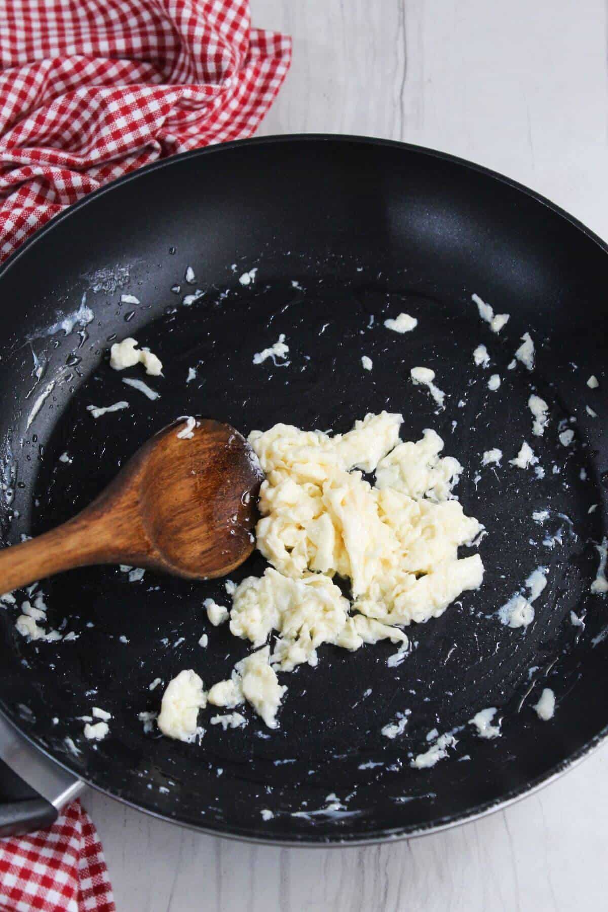 A frying pan with a wooden spoon and scrambled egg.