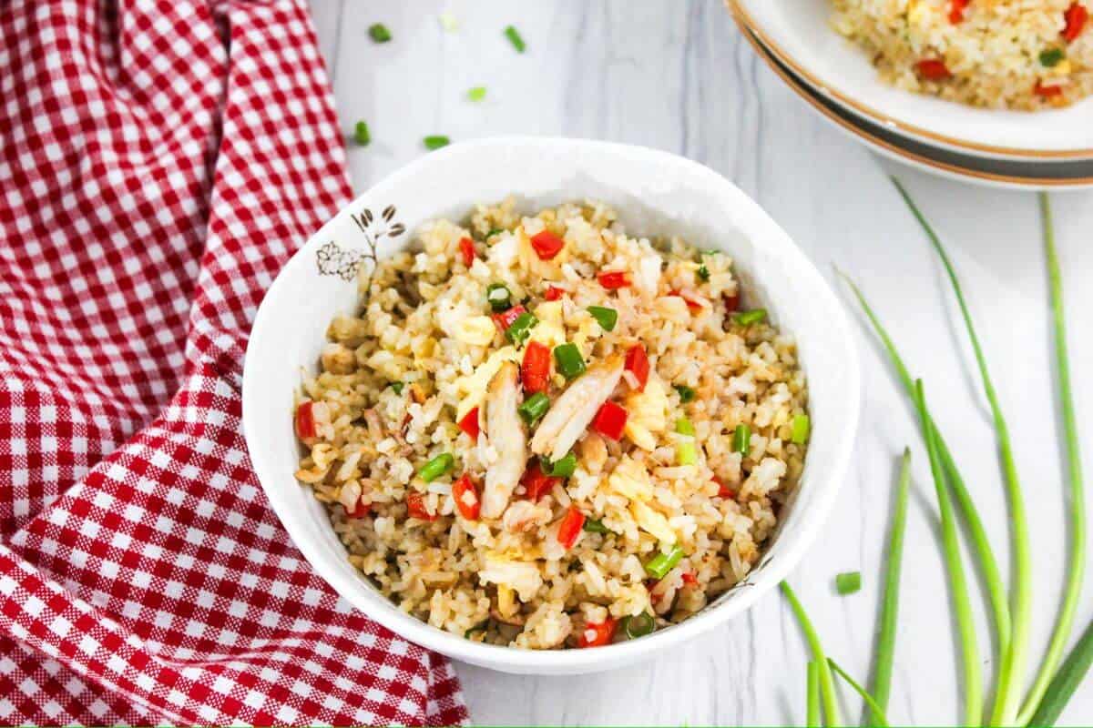 Crab fried rice in a white bowl on a red and white checkered tablecloth.