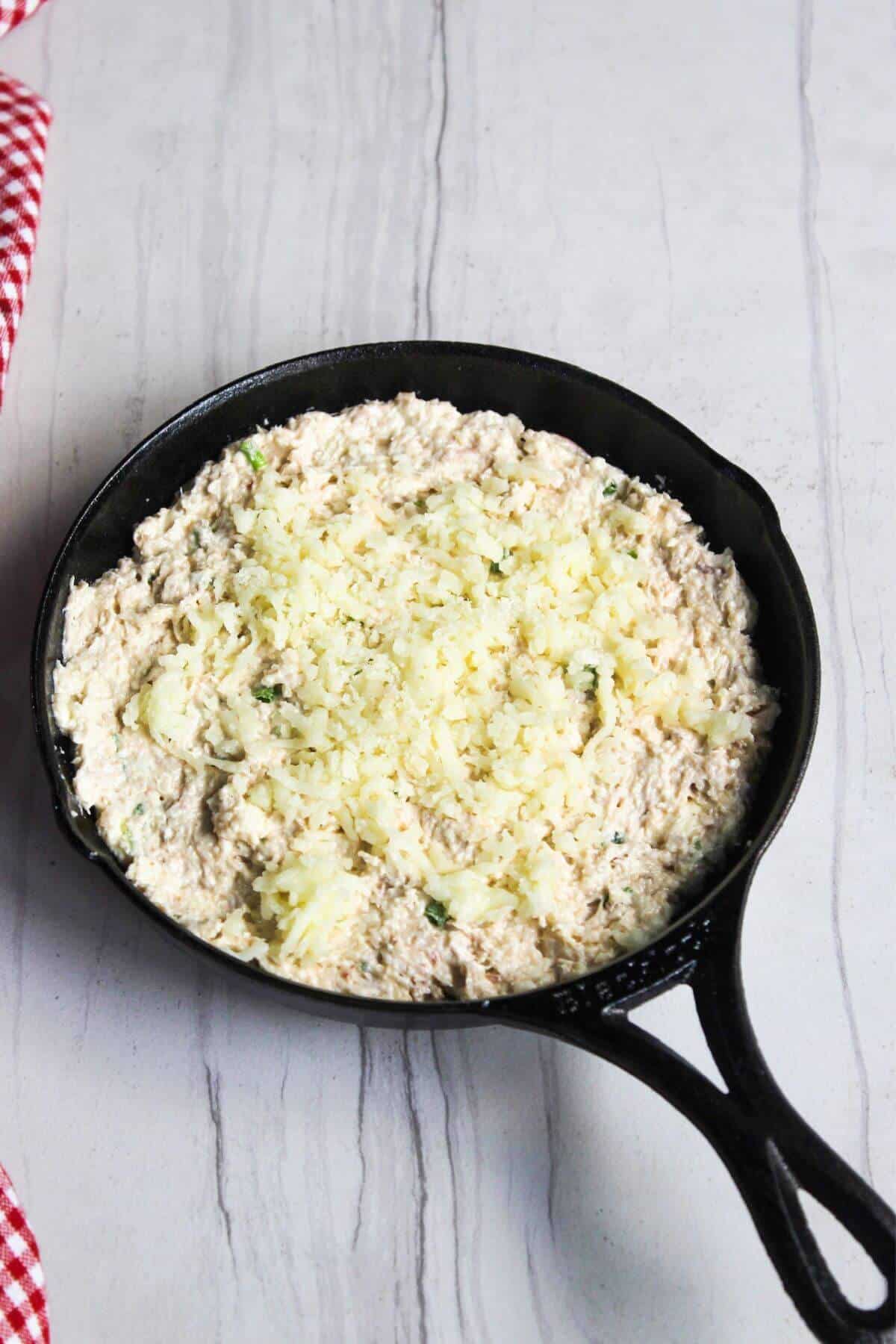 A skillet filled with crab dip mixture topped with mozzarella cheese.