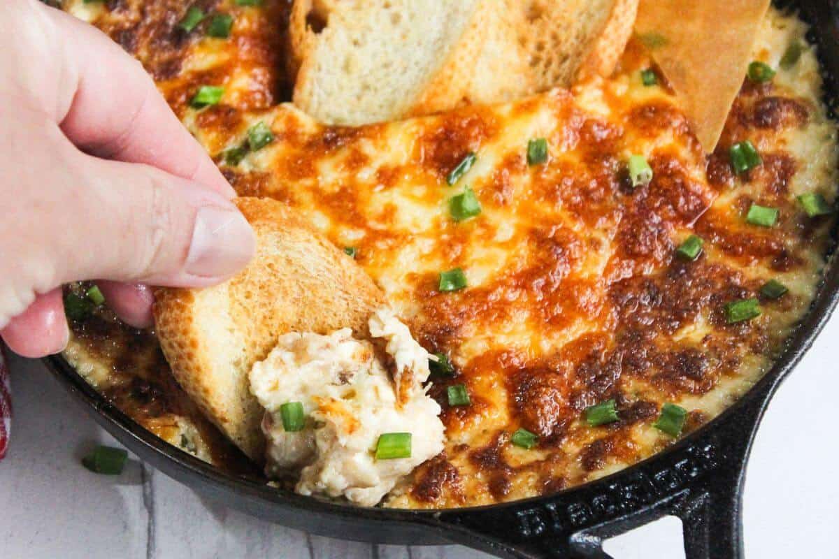 A person dipping bread into a skillet of cheesy dip.