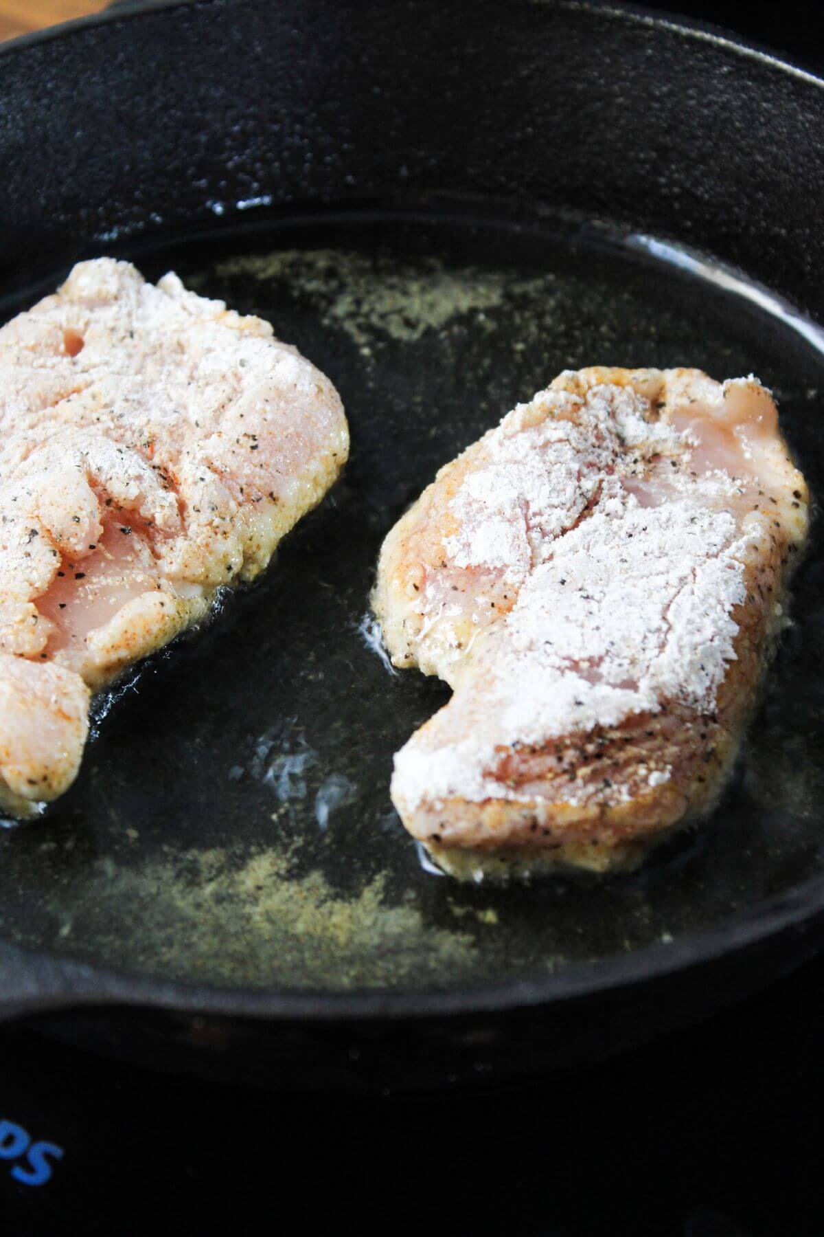 Two pieces of chicken are being cooked in a frying pan.