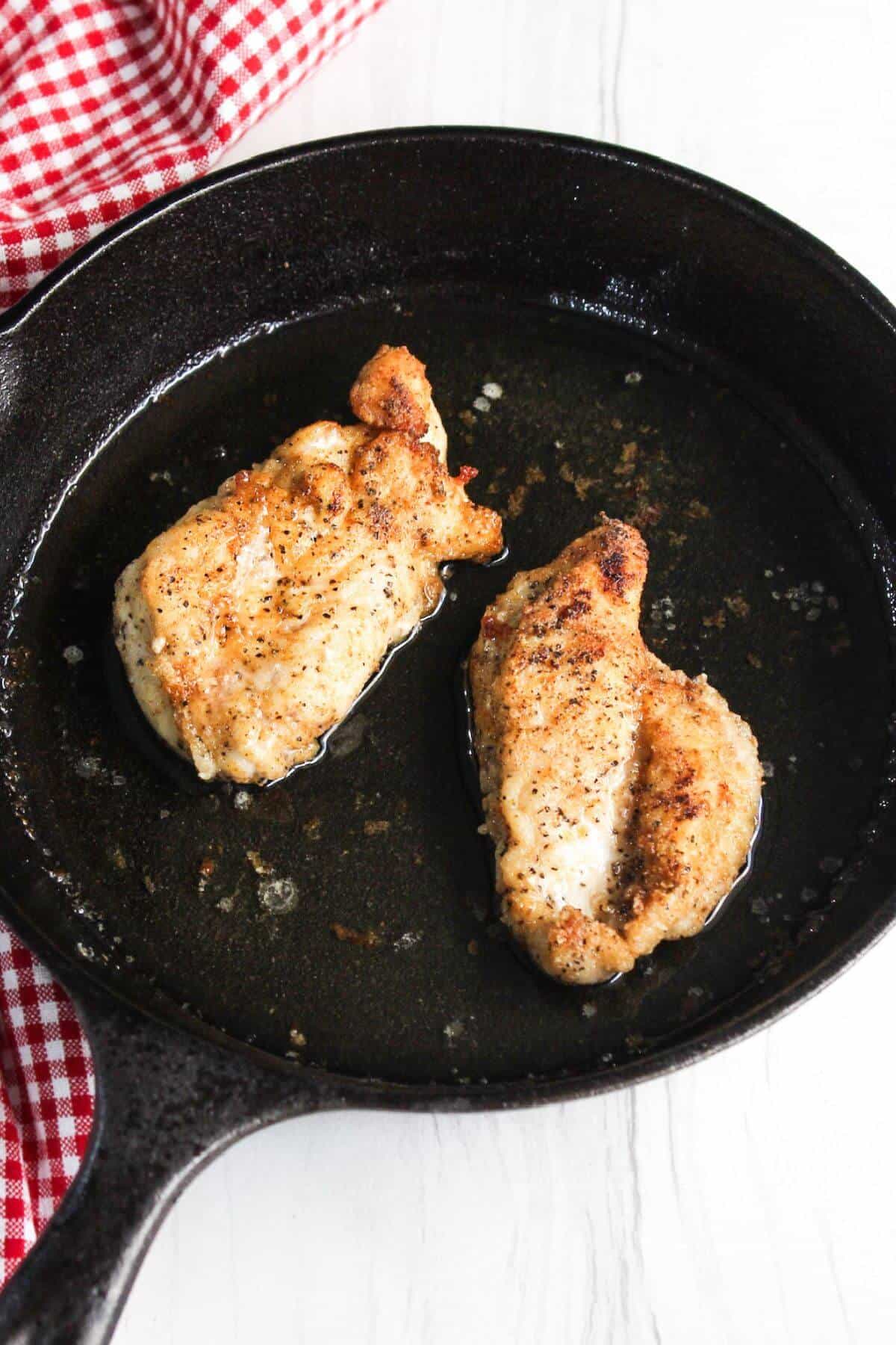 Two fried chicken breasts in a cast iron skillet.