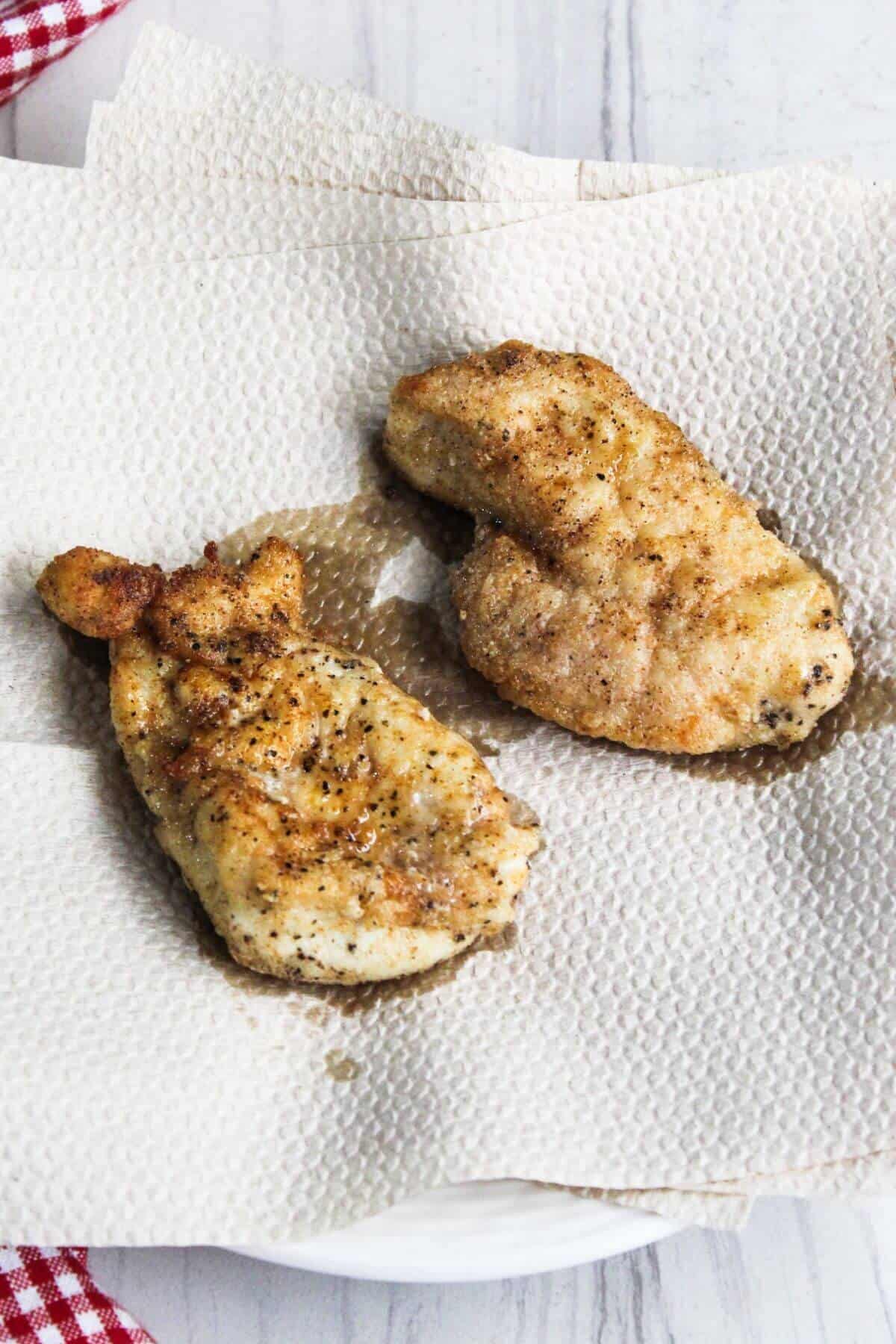 Two fried chicken breasts on a napkin next to a checkered napkin.