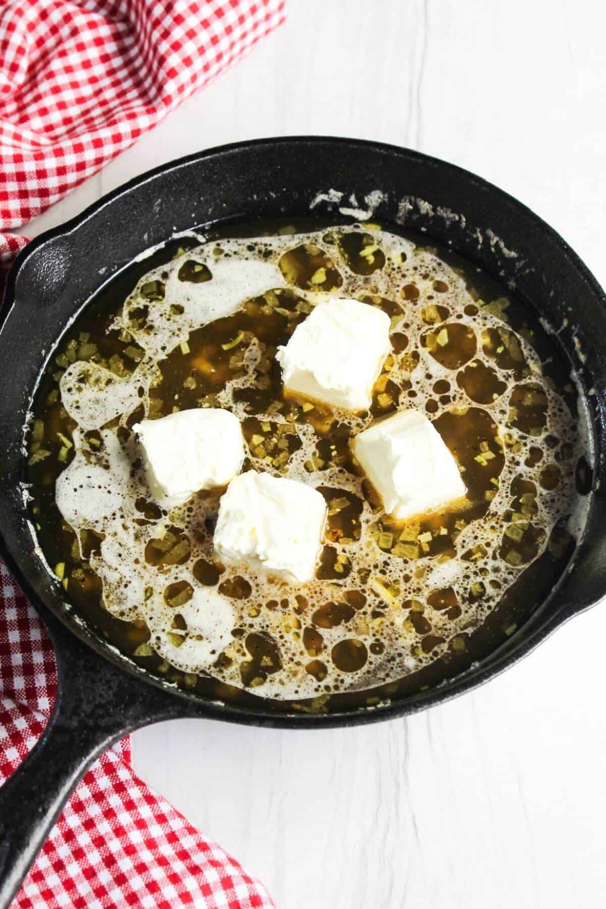 A cast iron skillet with butter pieces in it.