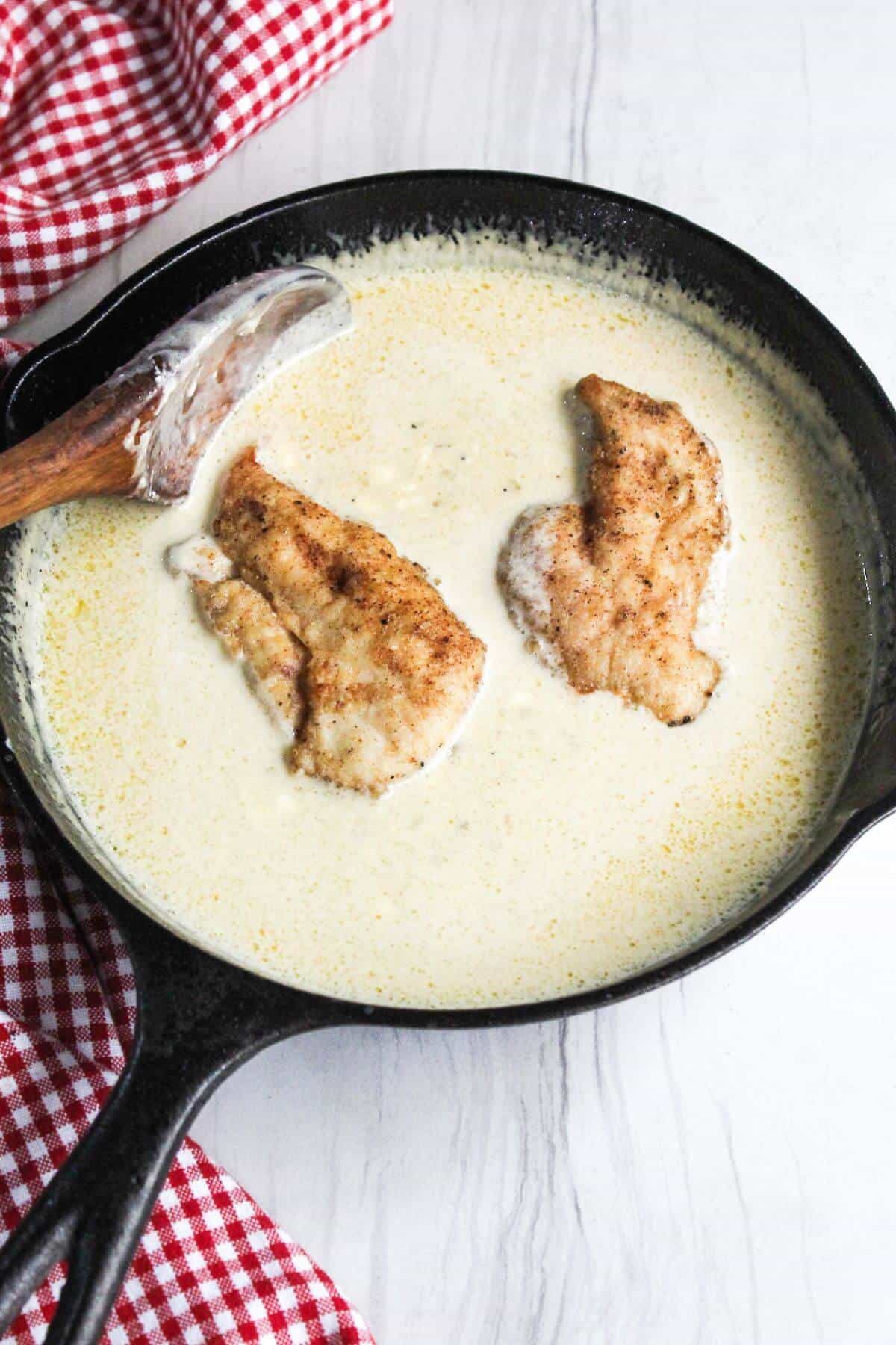 A skillet full of chicken in a creamy sauce with a wooden spoon.