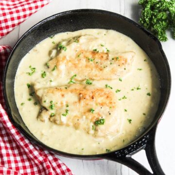 Chicken breasts in a skillet with cream cheese sauce and parsley.