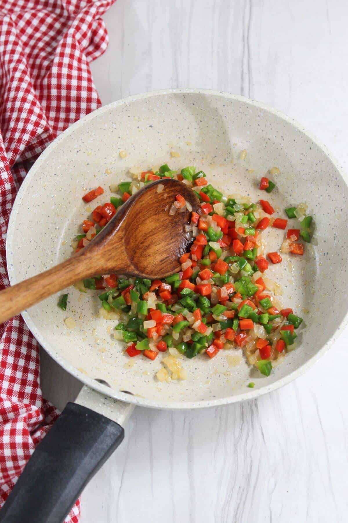 A frying pan with peppers and a wooden spoon.