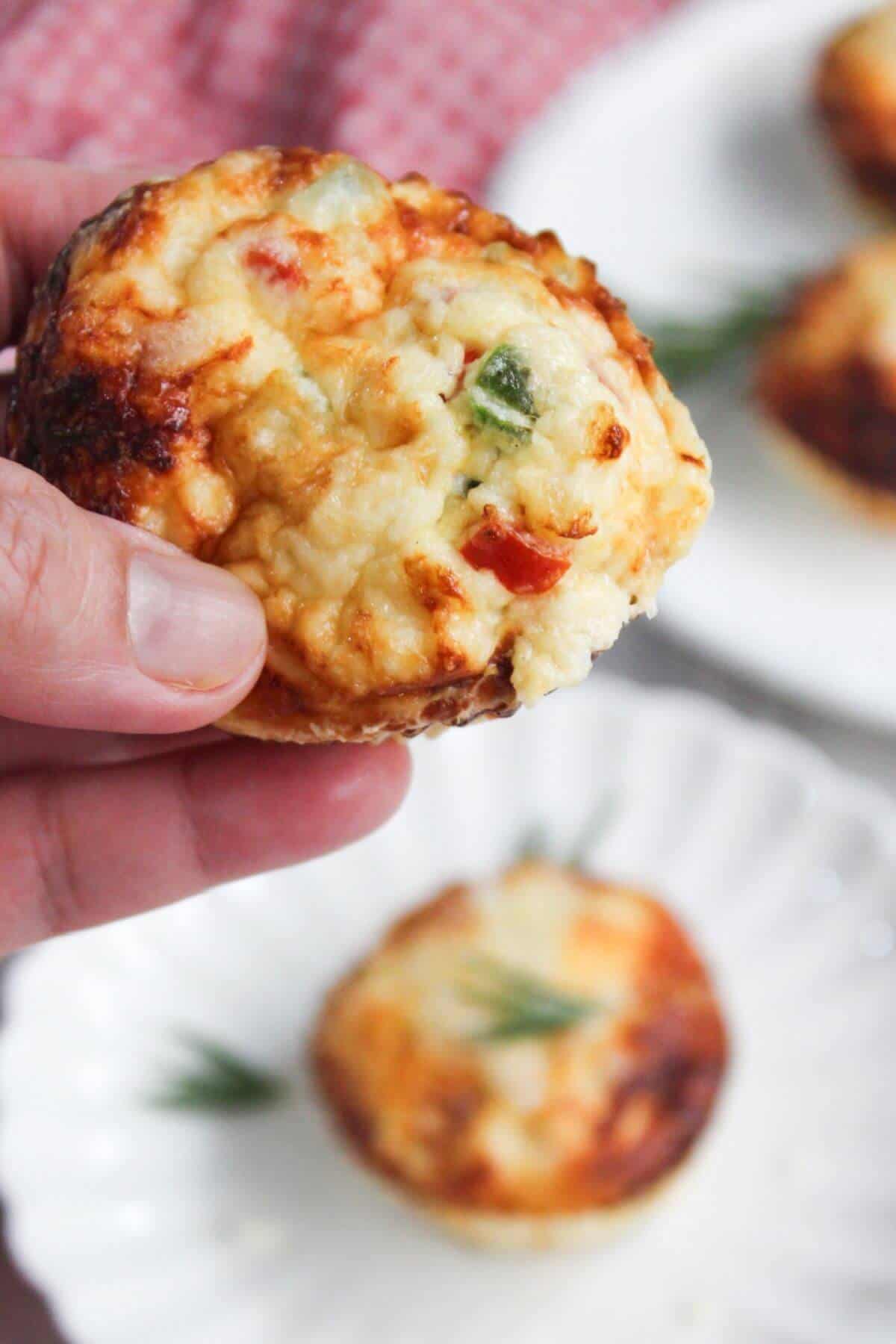 A hand holding a small cheese and vegetable egg white frittata muffin.