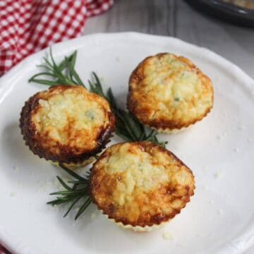 Three egg white frittata muffins on a white plate with a sprig of rosemary.