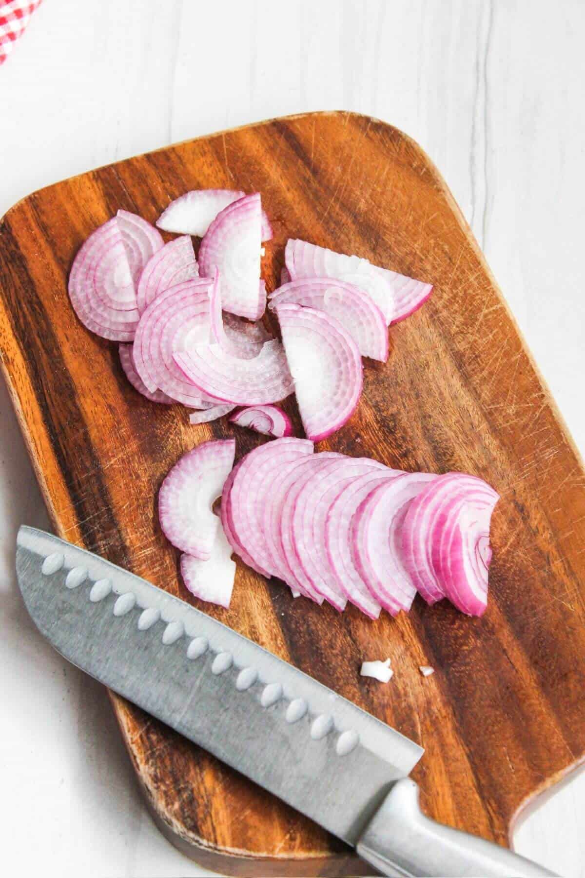 Sliced red onions on a cutting board with a knife.