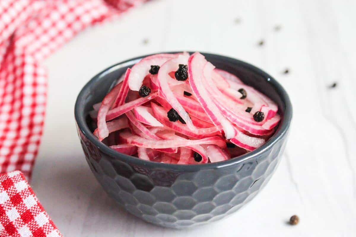 Pickled red onions in a bowl with black pepper.