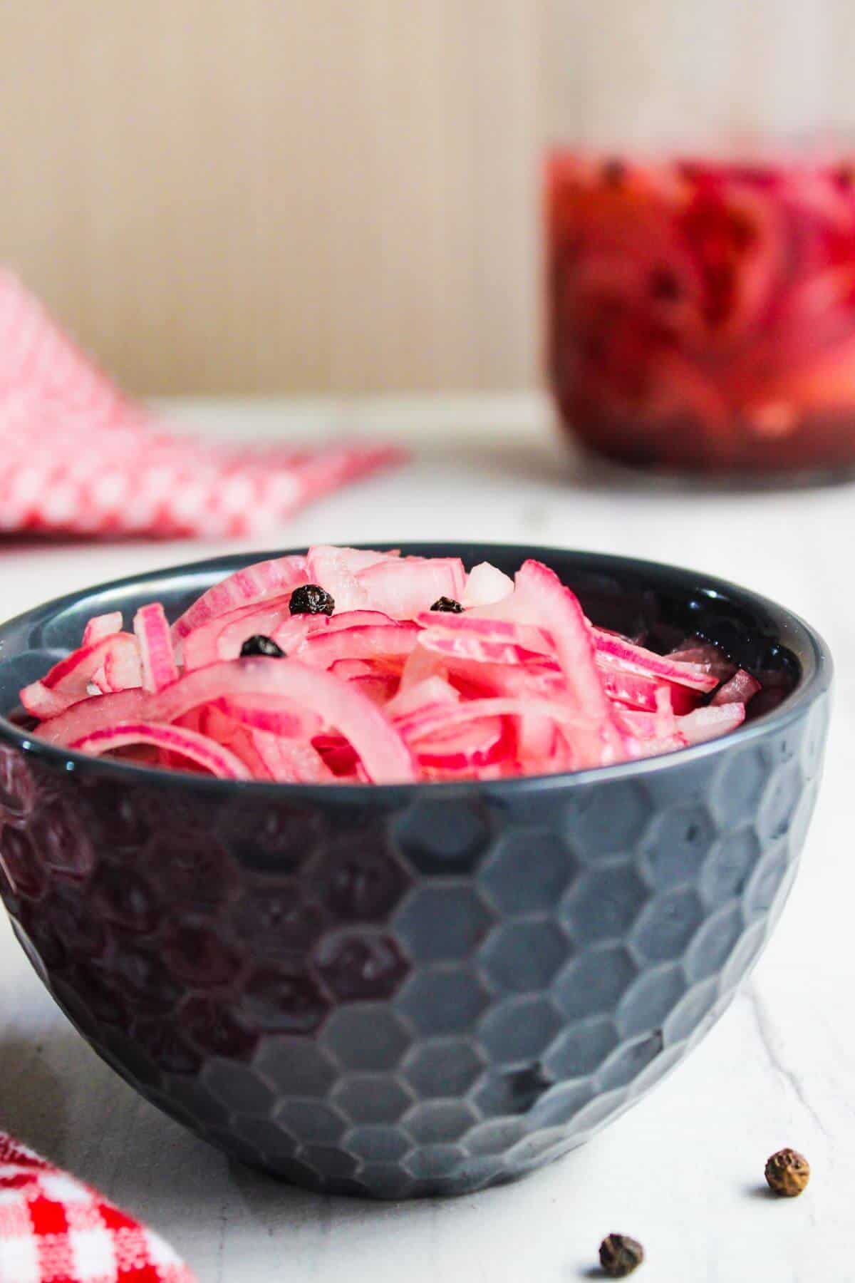 A bowl of sliced red onions next to a bottle of pickled onions.
