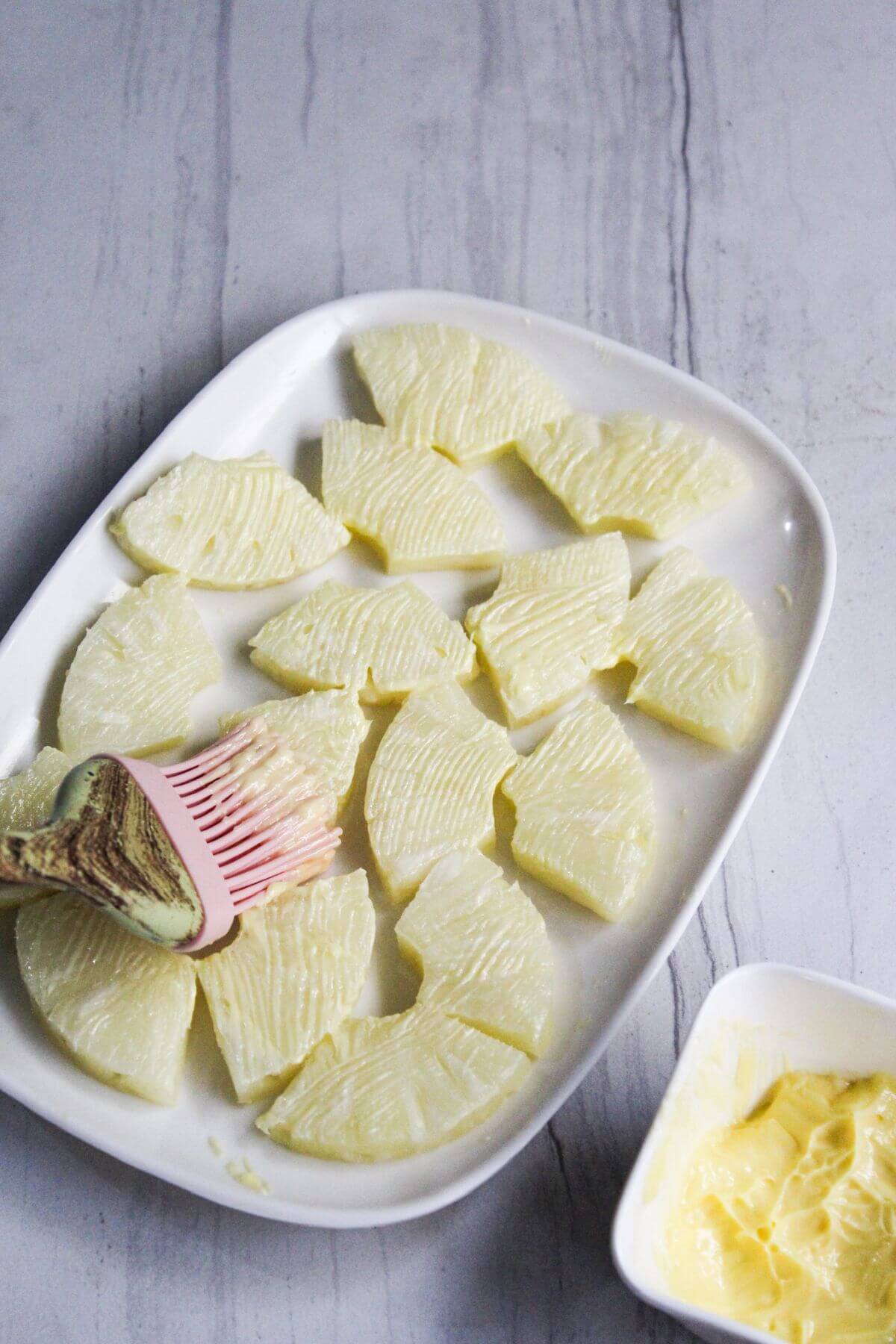 A white plate with sliced pineapple getting butter brushed on.