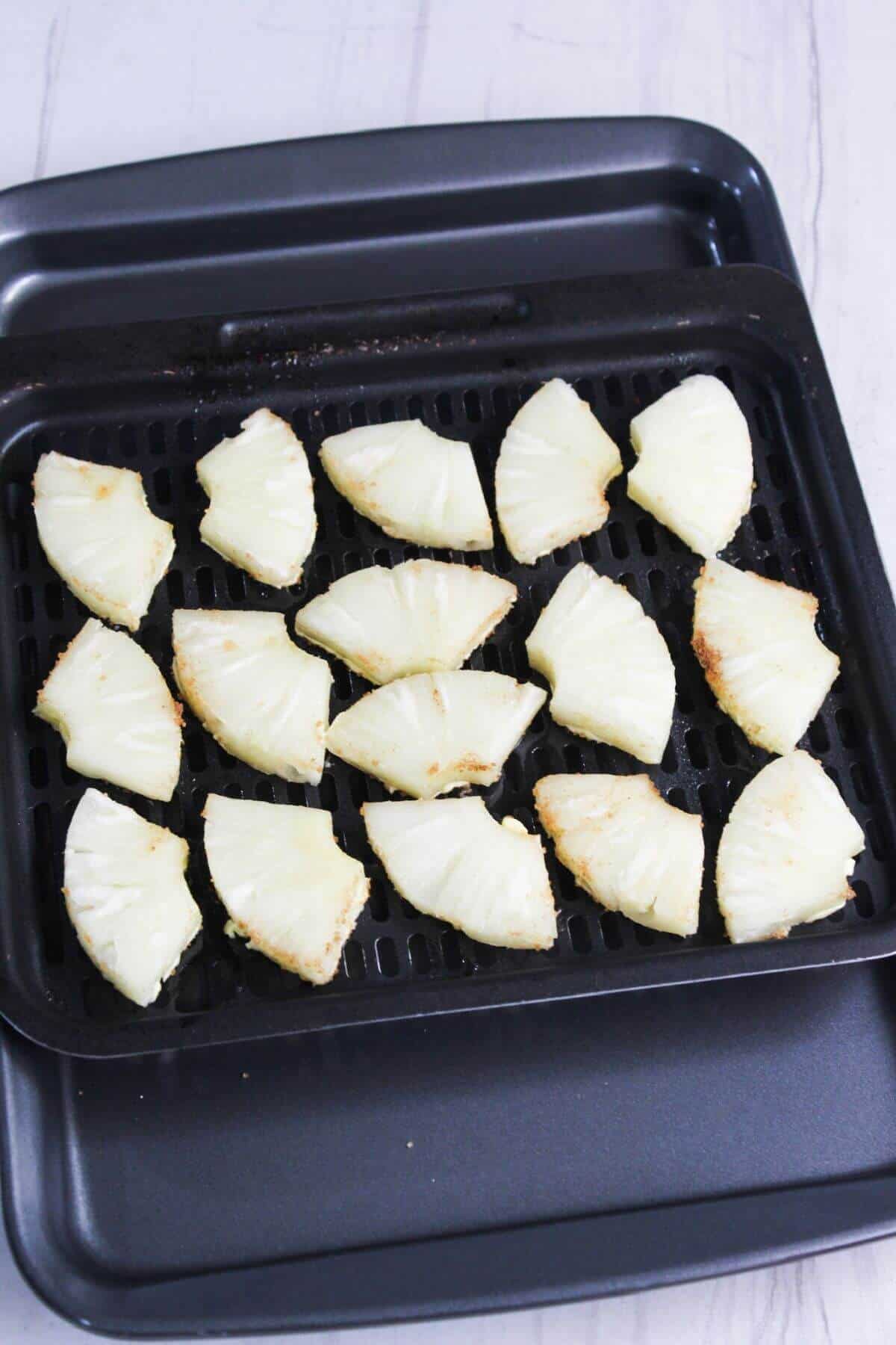 Sliced pineapple on a an air fryer tray.