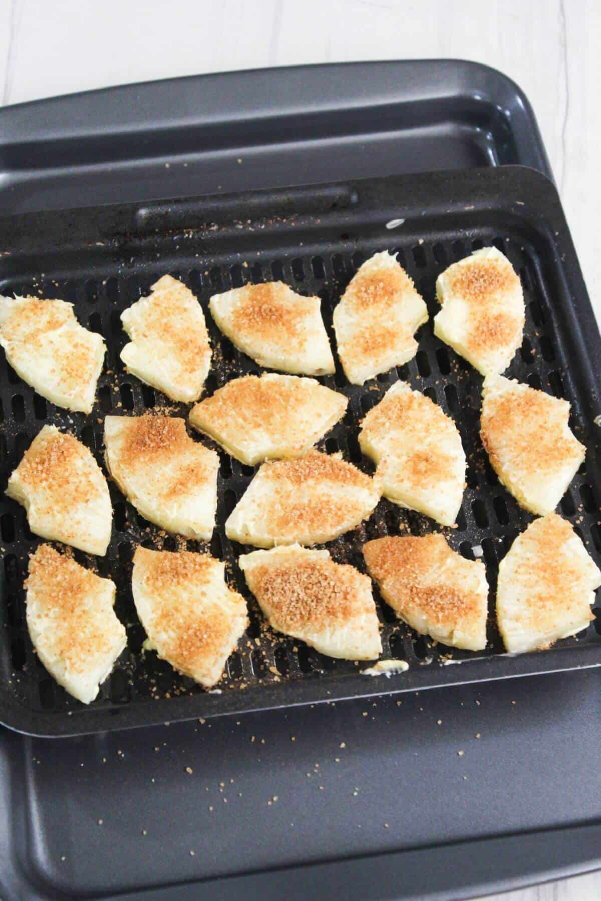 An air fryer tray with pieces of pineapple coated in brown sugar on it.