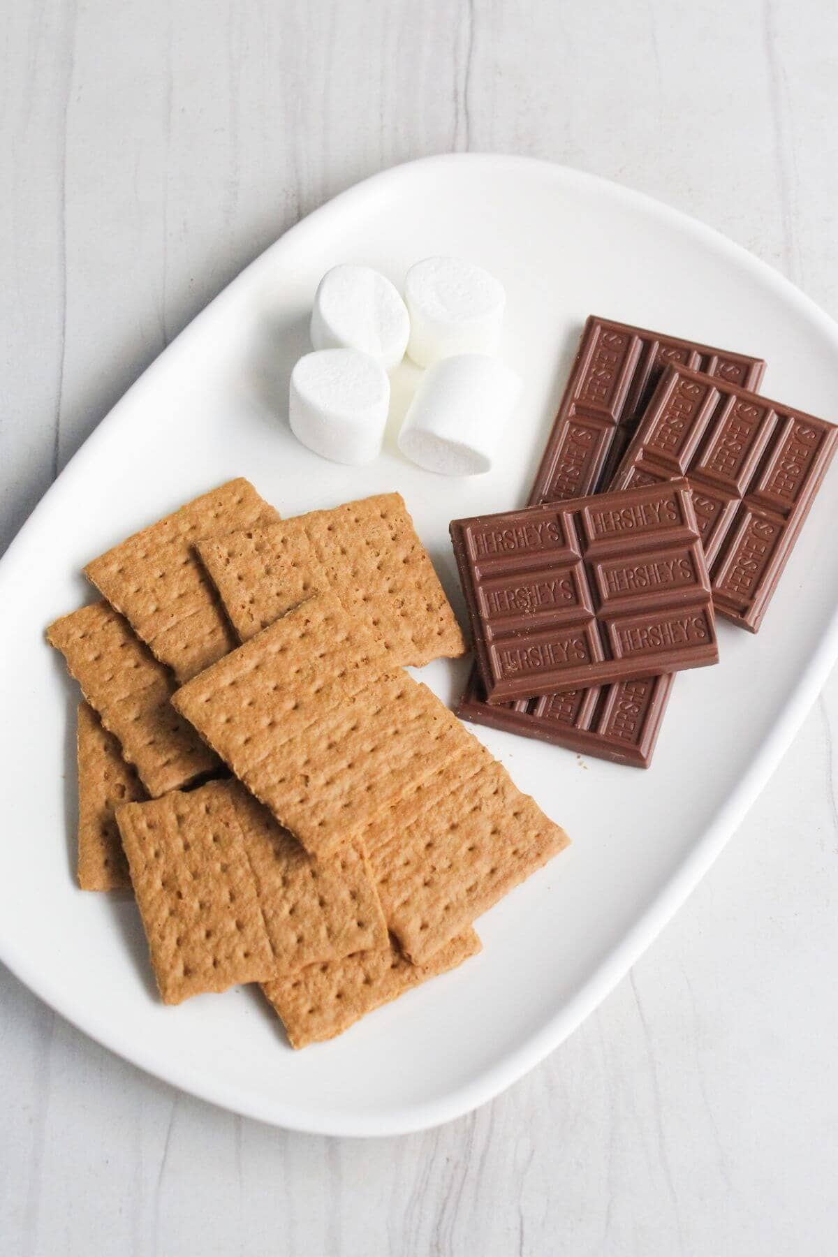 Graham crackers, marshmallows and chocolate bars on a white plate.