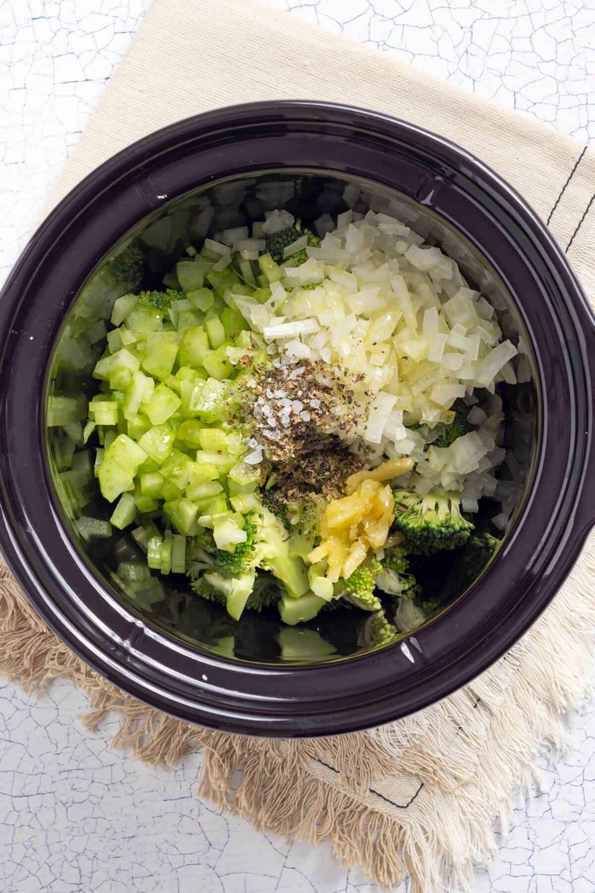 A black crock pot filled with broccoli, onions, and seasonings.