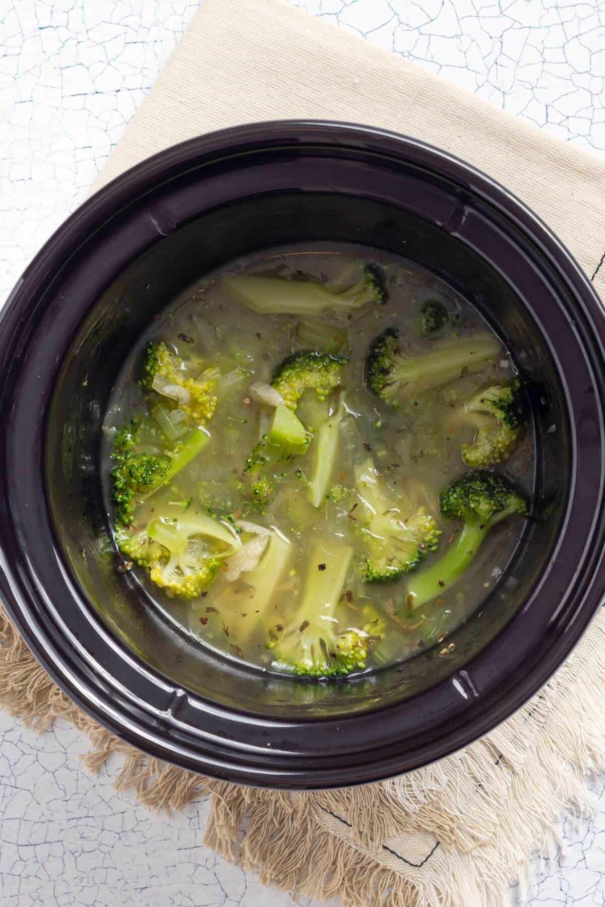 A crock pot of soup with broccoli in it.