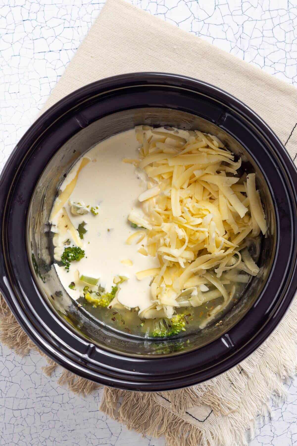 A crock pot with cheese and cream in it.